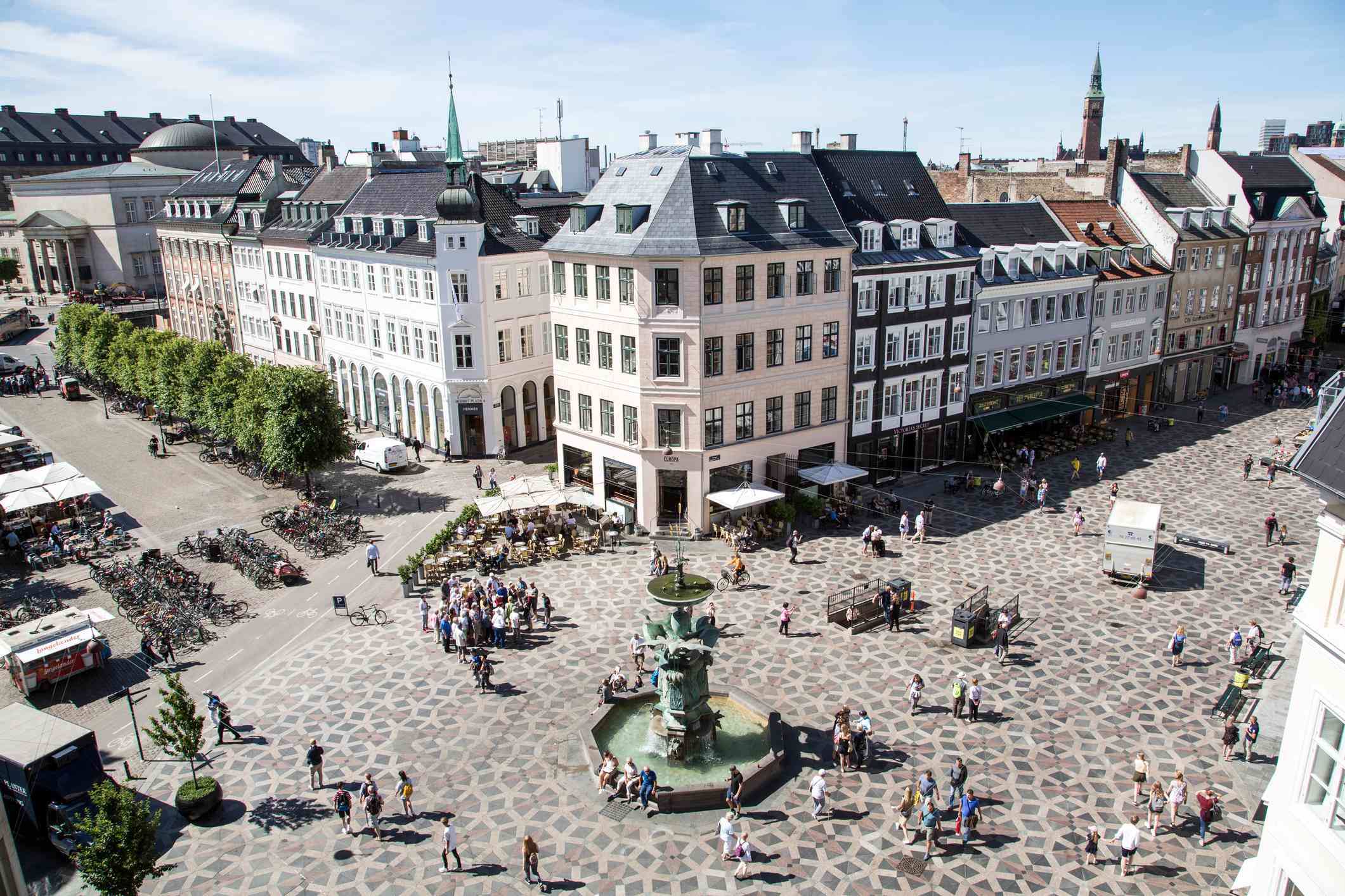 vista aérea de una zona comercial con amplias pasarelas de azulejos decorativos que rodean una fuente verde en Strøget, Copenhague