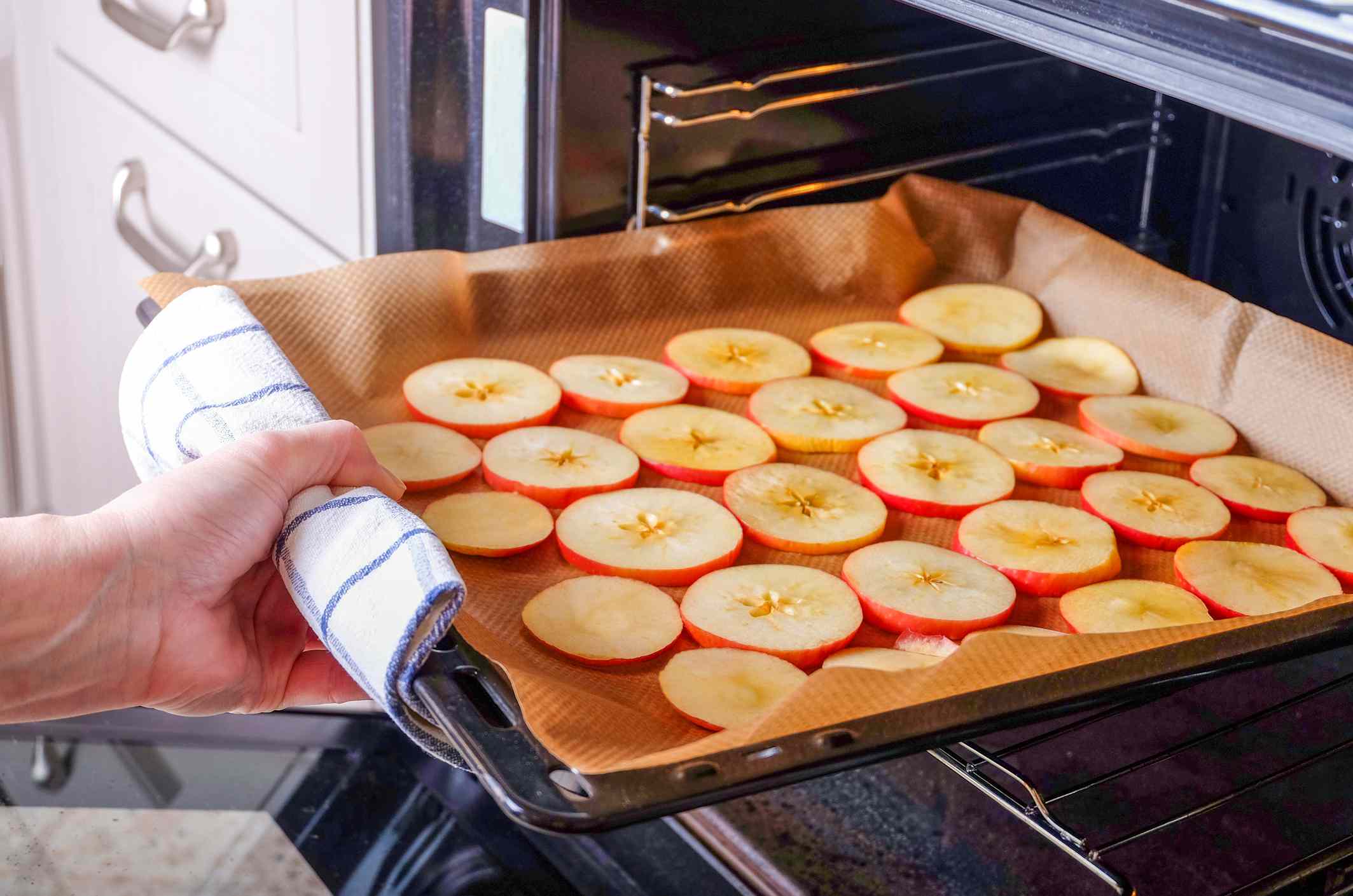 Una persona mete una bandeja de manzanas cortadas en rodajas en un horno eléctrico para que se sequen