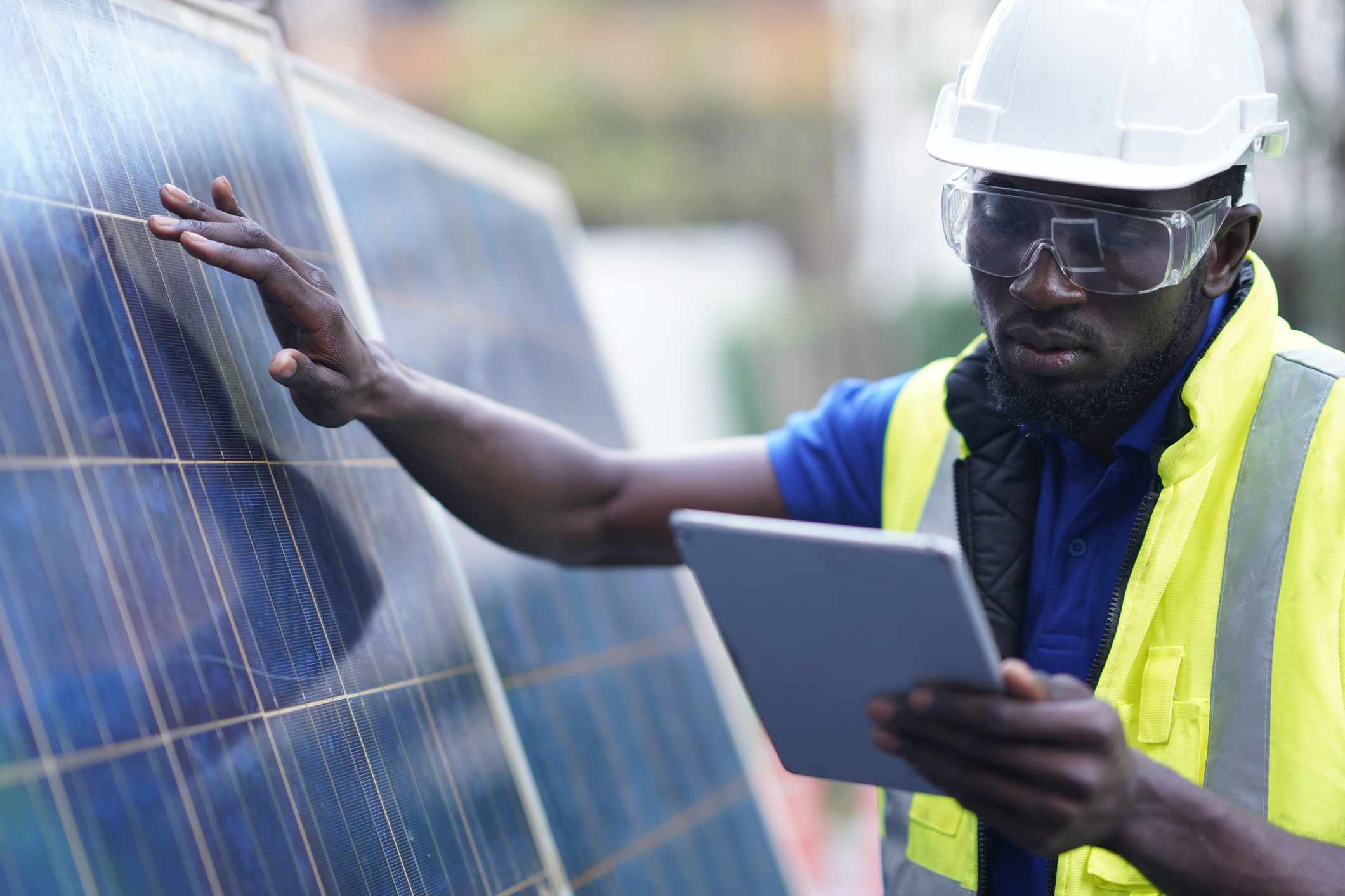 Un ingeniero de sistemas de energía solar de ascendencia africana con gafas de seguridad y casco blanco realiza un análisis de la eficiencia energética de los paneles solares