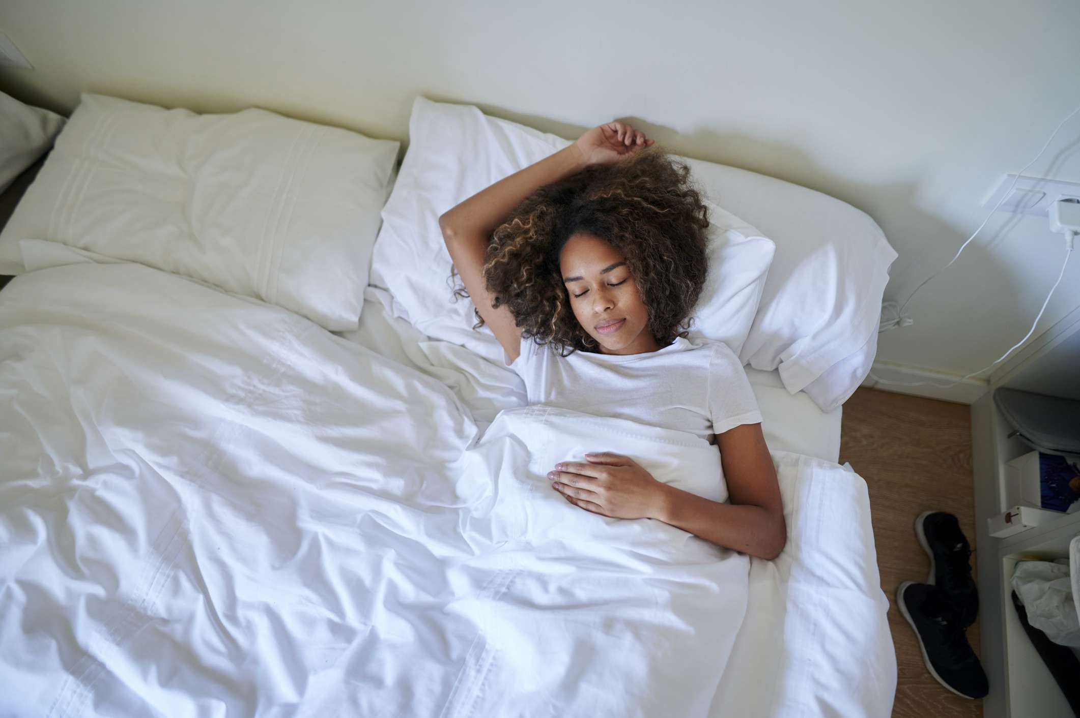 mujer dormida con el pelo rizado tumbada en la cama blanca con los brazos extendidos