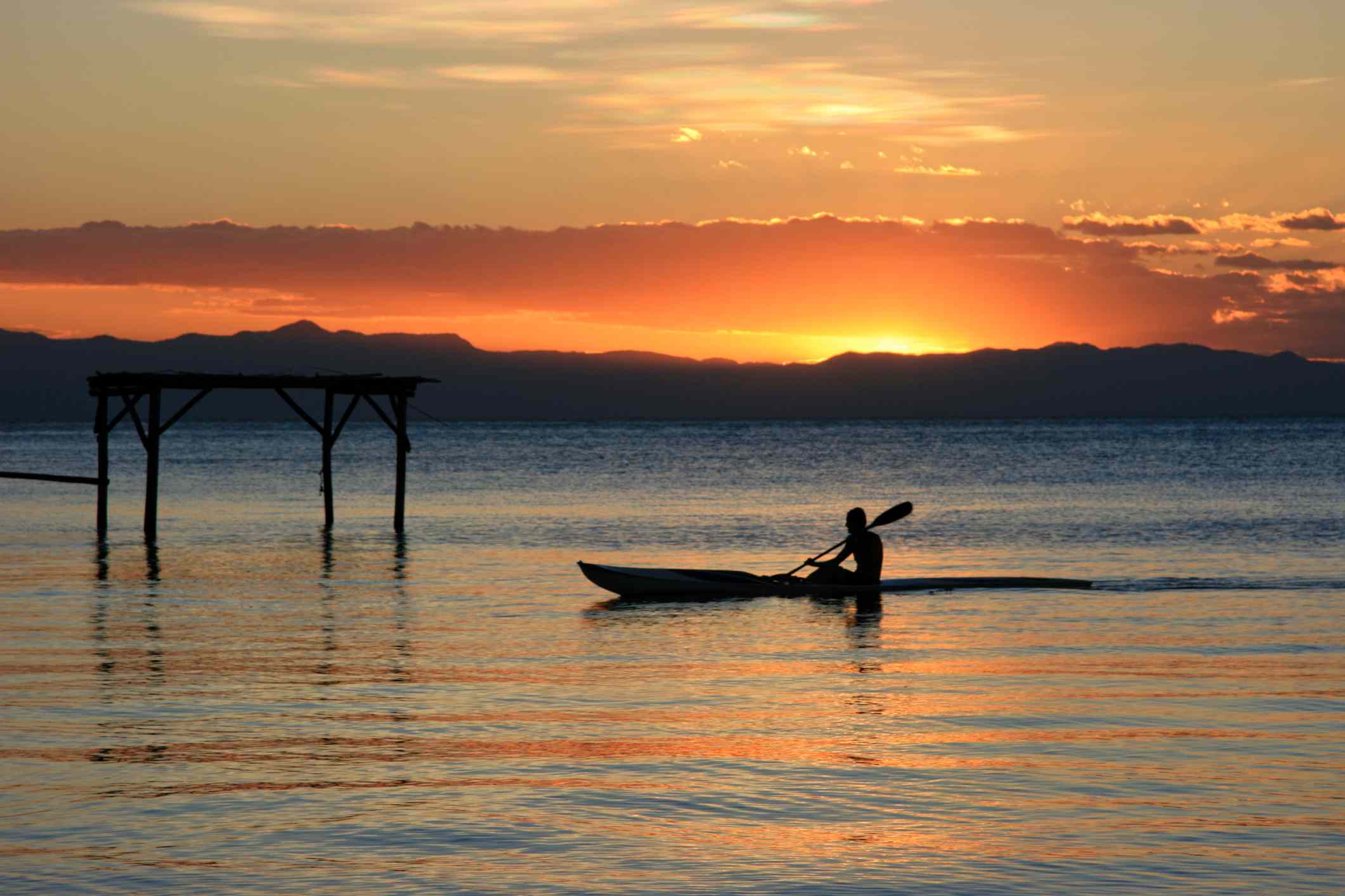 Un solo kayakista en el lago Malawi con una vívida puesta de sol naranja y amarilla en la distancia