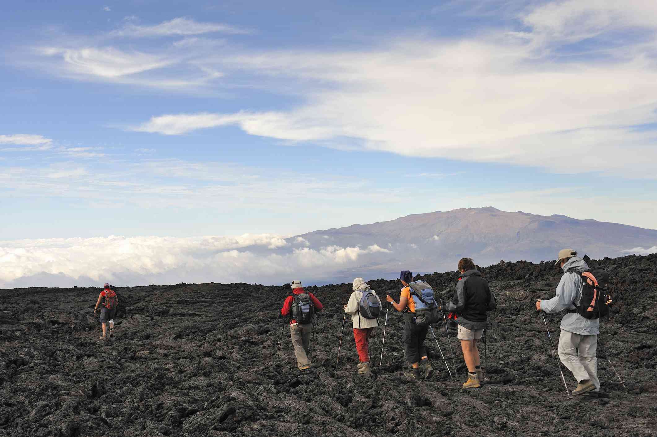 Personas caminando sobre lava enfriada; el volcán Mauna Loa al fondo