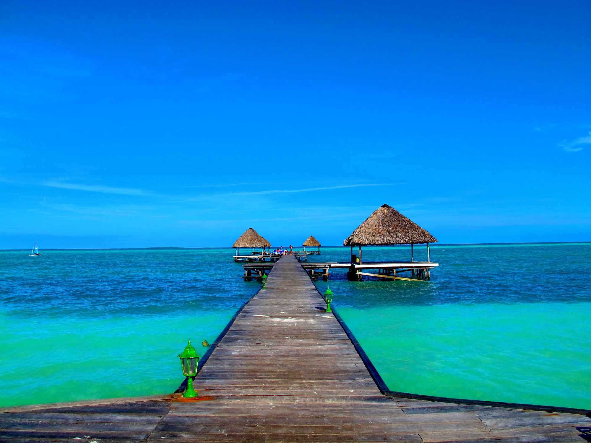 muelle de madera que conduce a tres cabañas con techo de paja sobre el agua azul y turquesa transparente bajo un cielo azul brillante en Cayo Coco