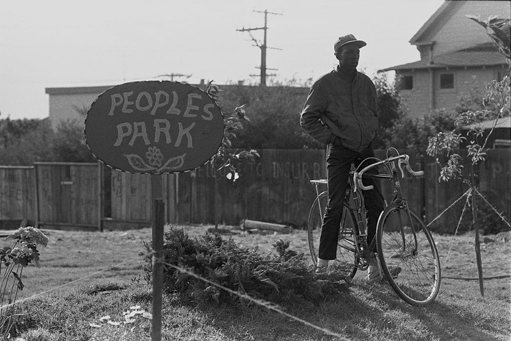 Un hombre con una bicicleta junto a un cartel en el Parque del Pueblo, Berkeley, CA.