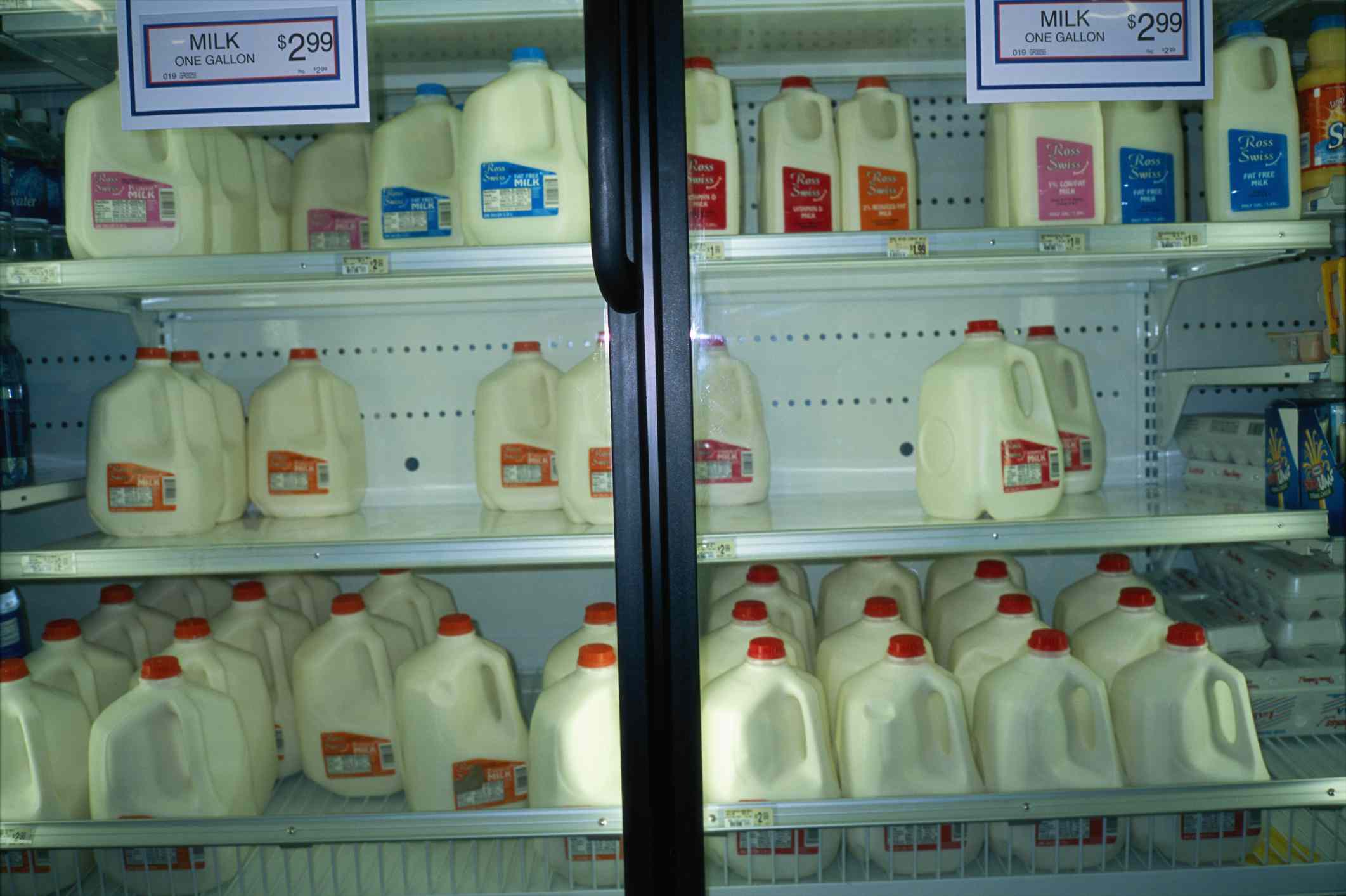 Cántaros de leche en un frigorífico de una tienda con carteles
