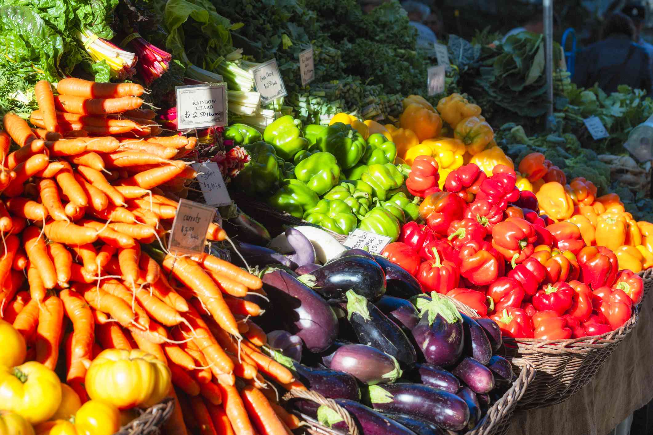 Primer plano del puesto del mercado agrícola con cestas de zanahorias, berenjenas y pimientos rojos, verdes y amarillos en un día soleado