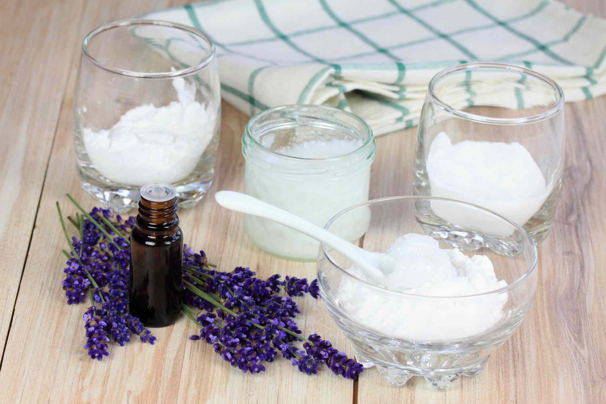 Un frasco de aceite esencial y vasos de cristal con ingredientes para un desodorante casero que incluye aceite de coco, bicarbonato de sodio y más