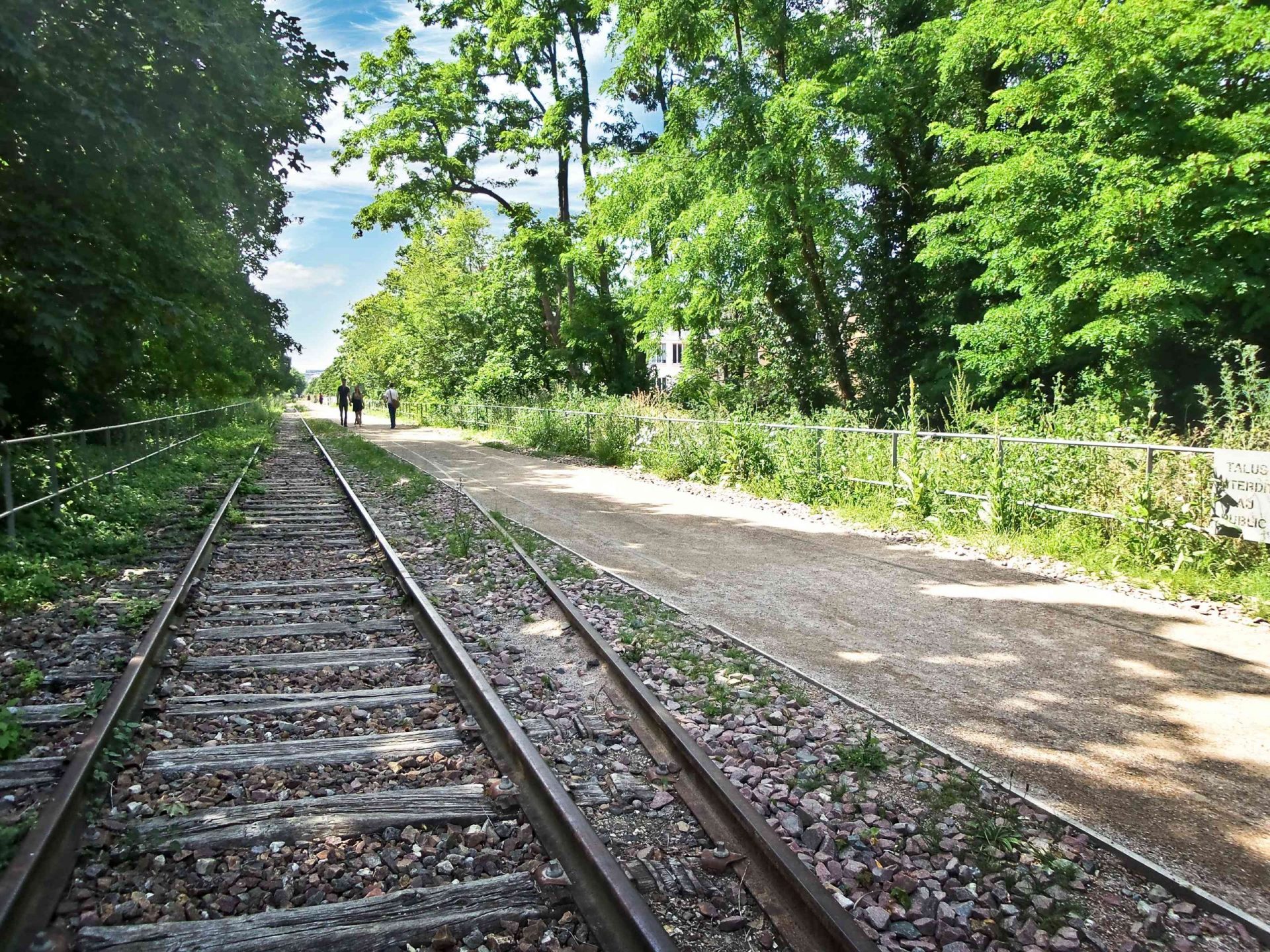 Una parte abandonada de la vía del tren junto a un sendero para caminar y altos árboles verdes que conforman la Petite Ceinture en Pari,