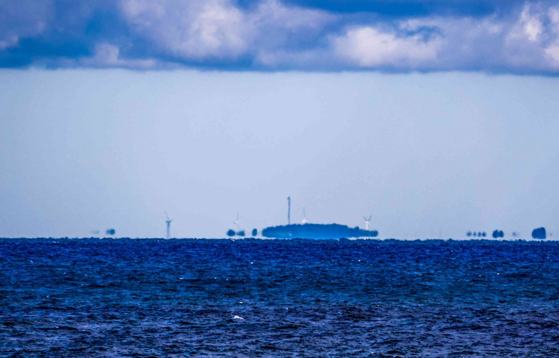 Vista desde el océano de un espejismo de Fata Morgana superior de la costa con turbinas de viento bajo un cielo nublado con algunas precipitaciones