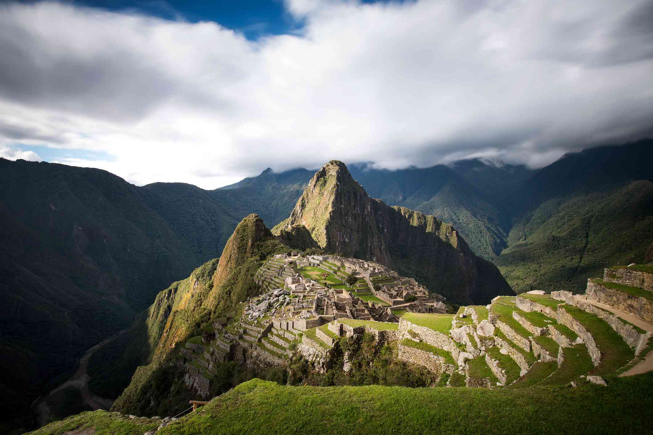 Vista de las montañas y ruinas de Machu Picchu cubiertas de exuberantes plantas verdes bajo densas nubes con un poco de cielo azul