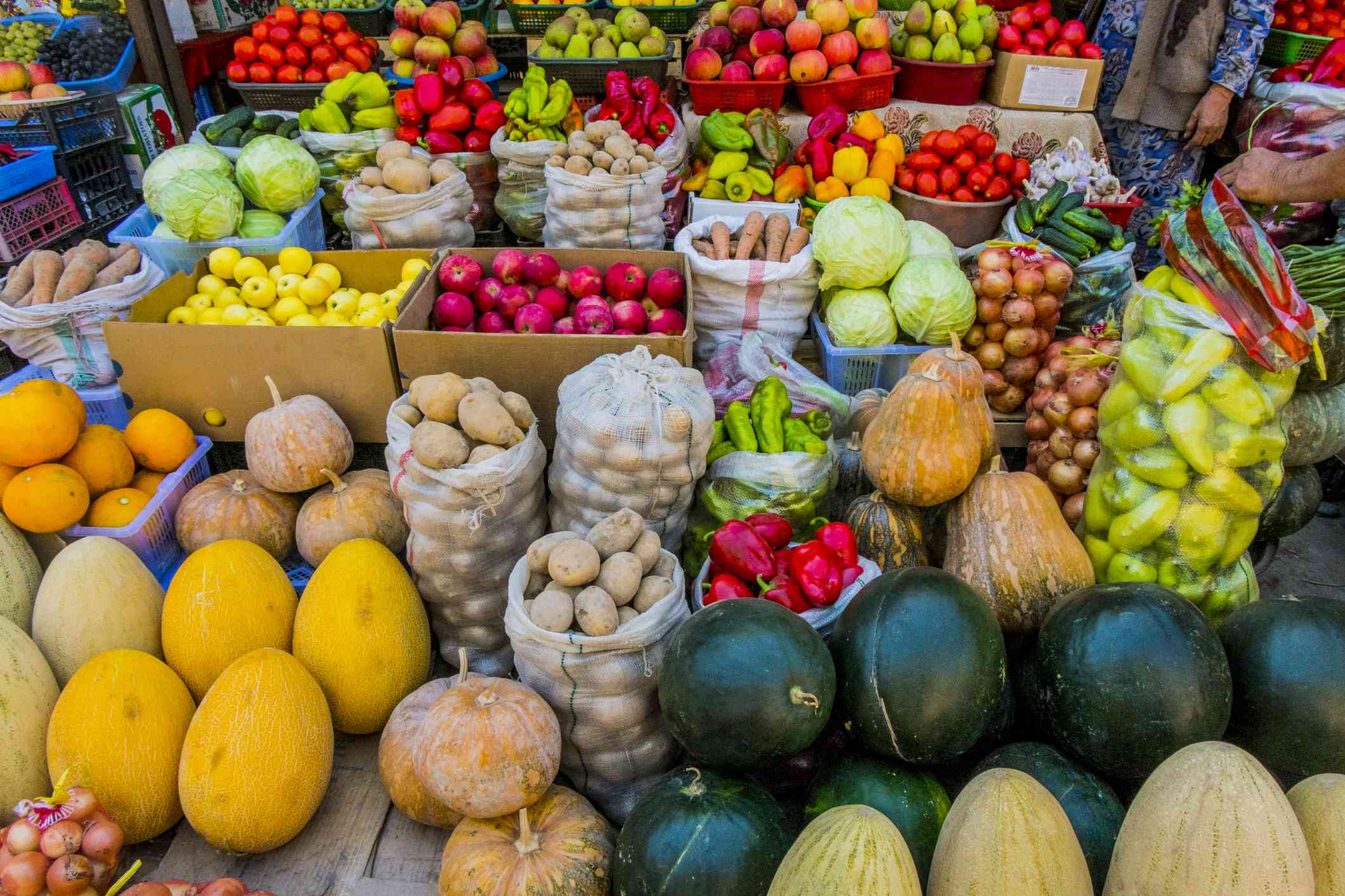 Variedad de frutas y verduras de colores, como melones, calabazas, tomates, patatas y manzanas, sobre mesas, en cajas y en bolsas en un mercado agrícola