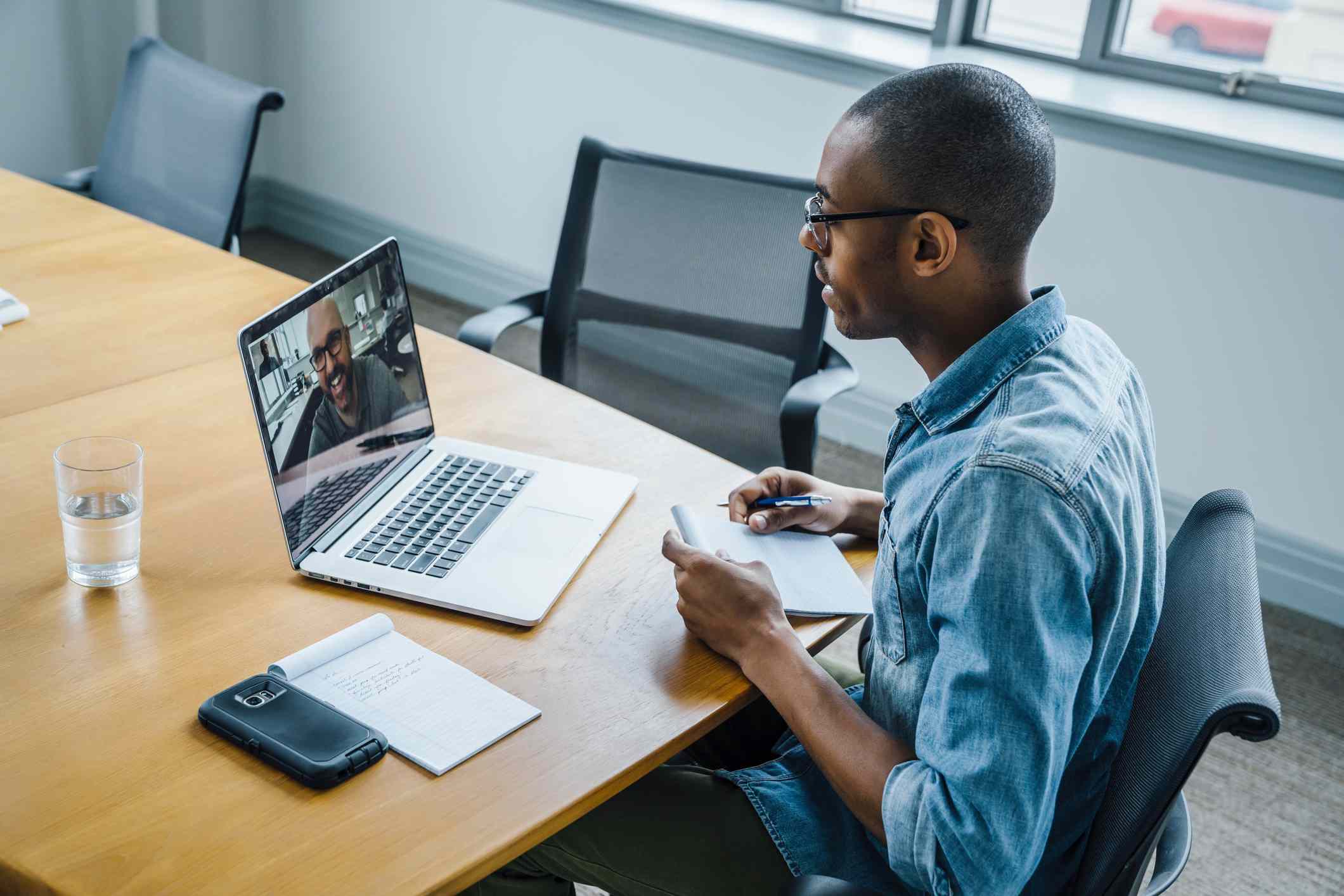Un hombre negro en una oficina tiene una reunión con zoom en un ordenador portátil