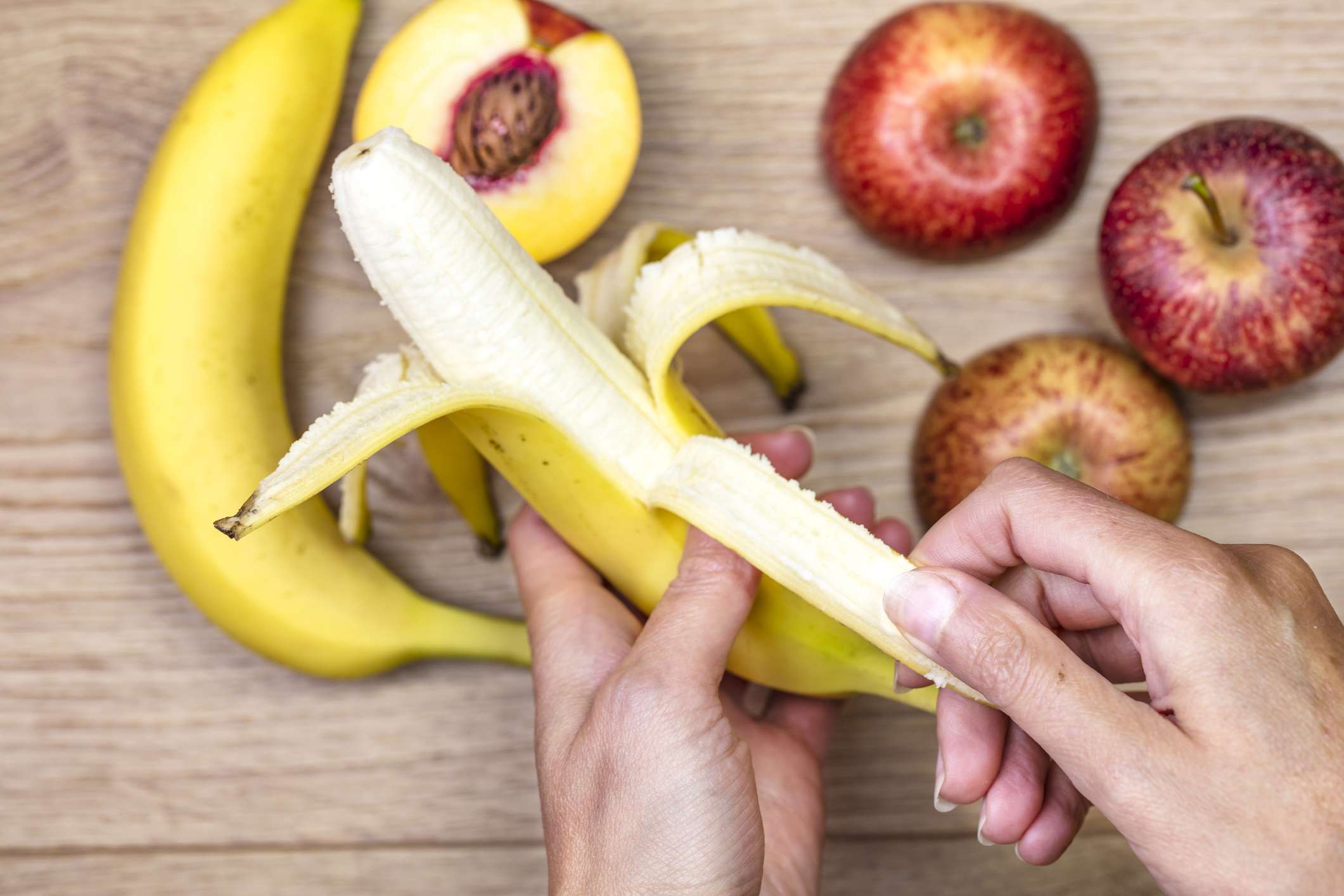 Una mano pelando un plátano sobre manzanas y melocotones