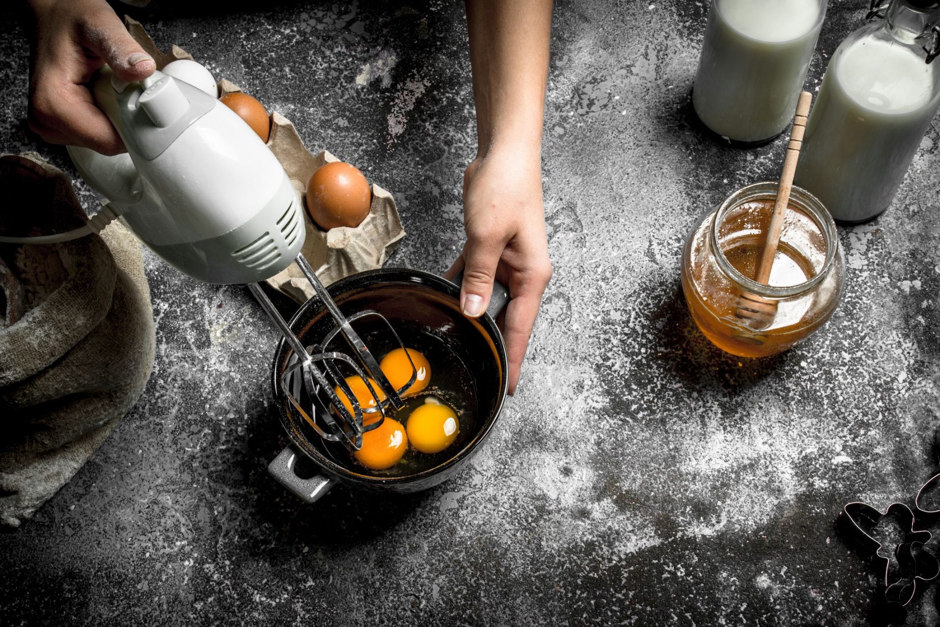 Persona batiendo huevos en una mesa con leche y miel