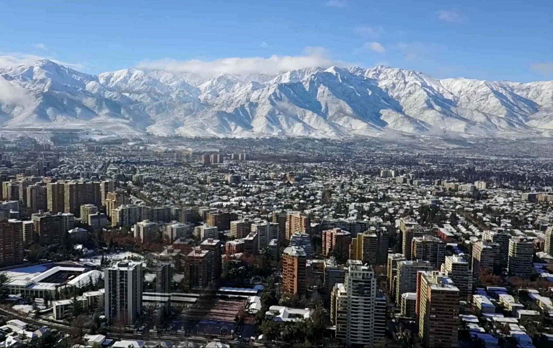 Rascacielos de Santiago en primer plano con montañas nevadas al fondo bajo un cielo azul