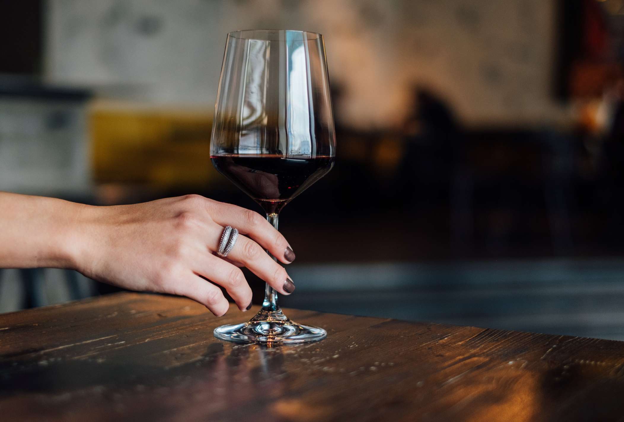 Una copa de vino tinto sostenida por una mano con uñas pintadas de color burdeos