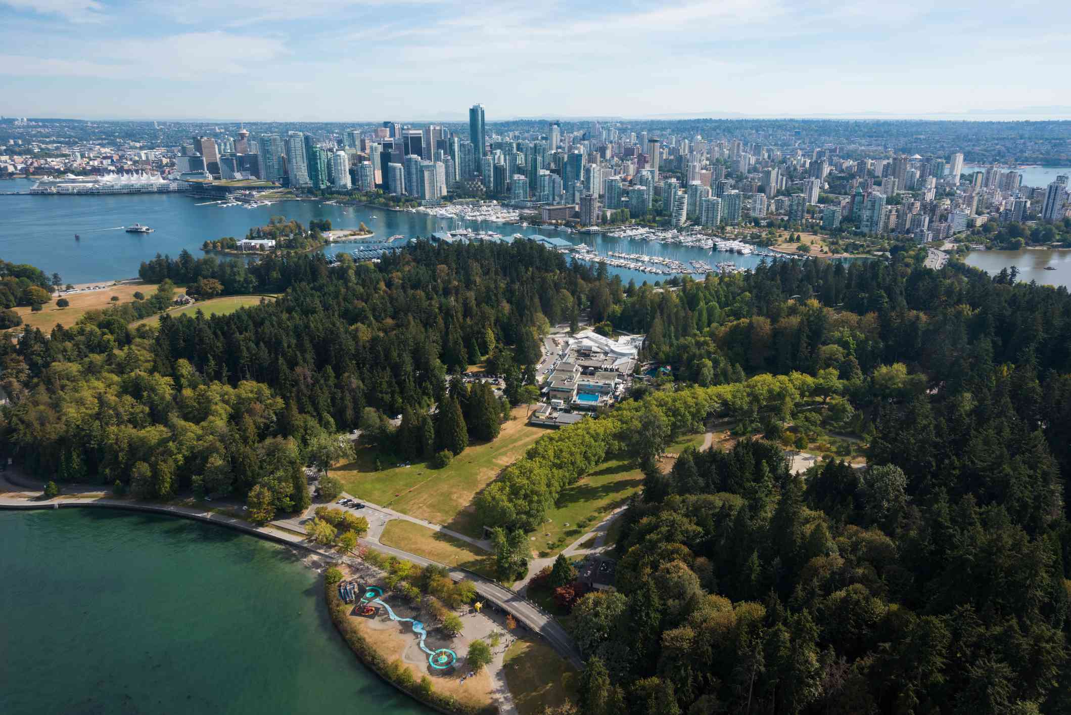 Vista aérea del Parque Stanley cubierto de frondosos árboles verdes y rodeado de agua con el centro de Vancouver al fondo