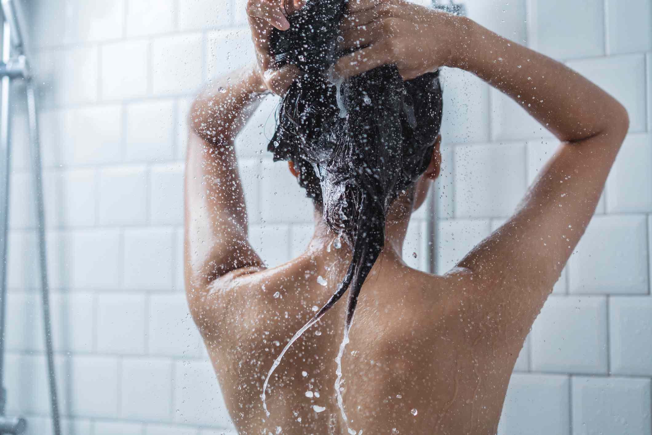 Una mujer lavándose el pelo en una ducha blanca