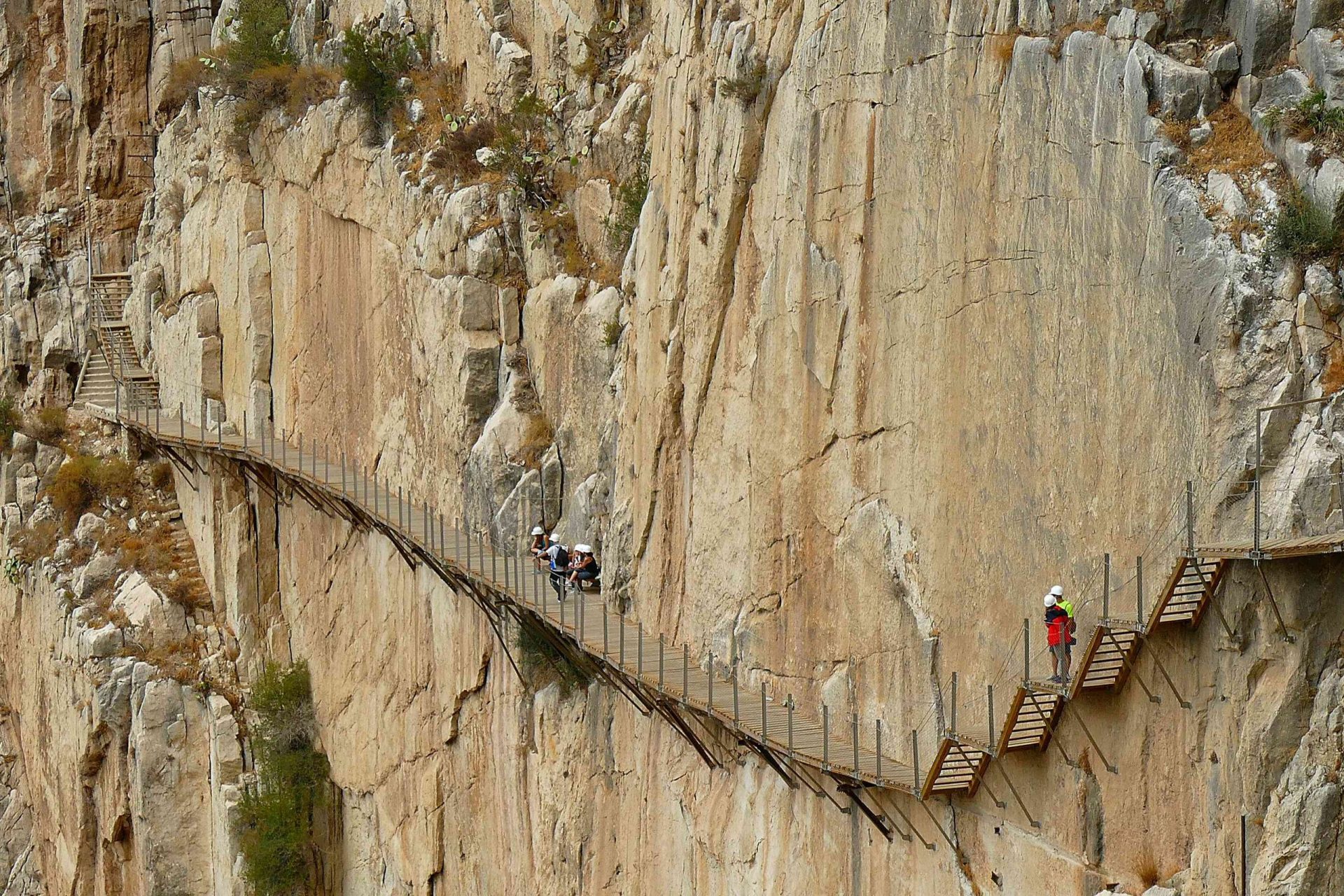 Excursionistas caminando por un estrecho puente a lo largo de un acantilado vertical