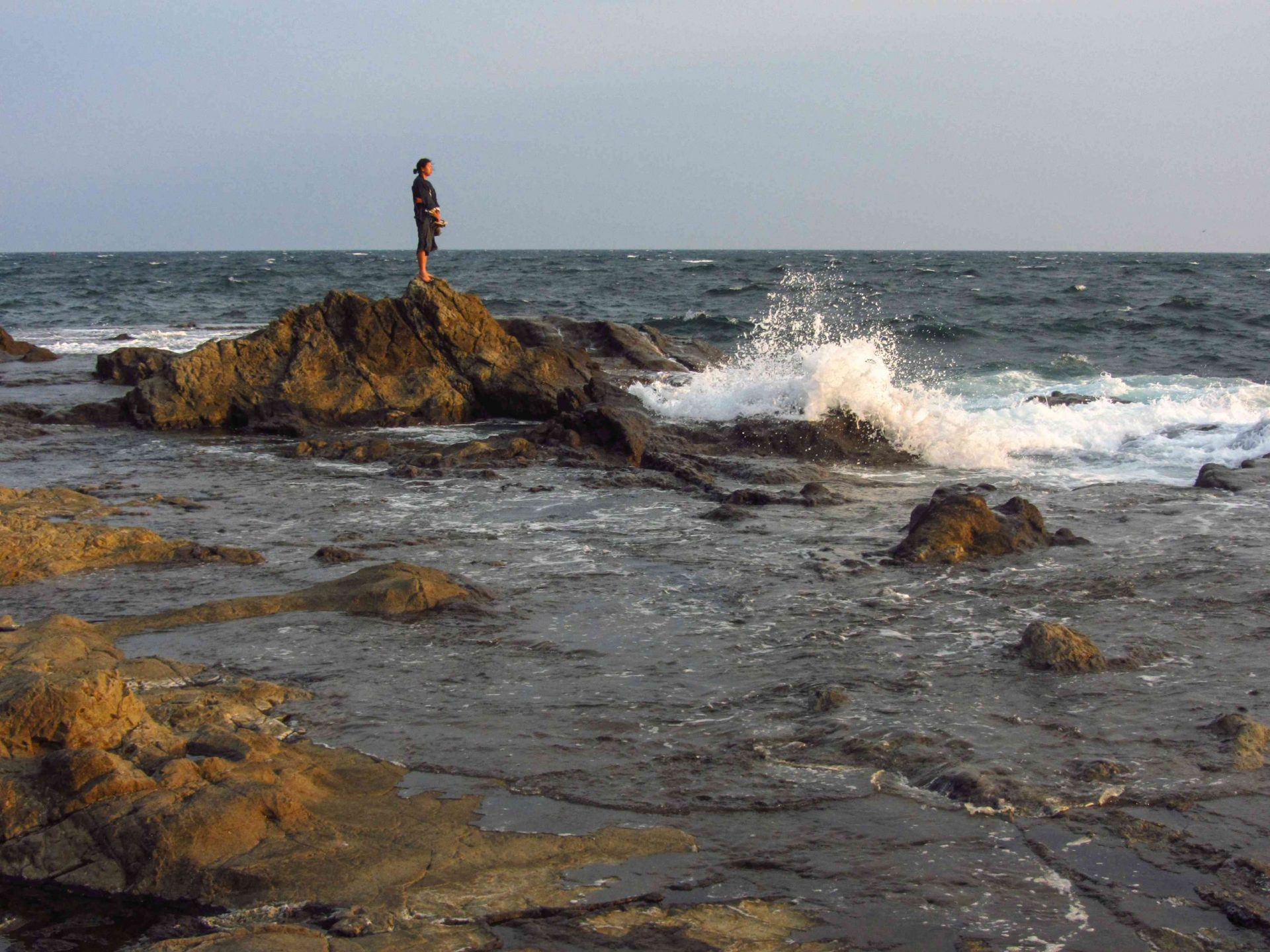 una persona está sola sobre una roca escarpada mientras las olas chocan a su alrededor