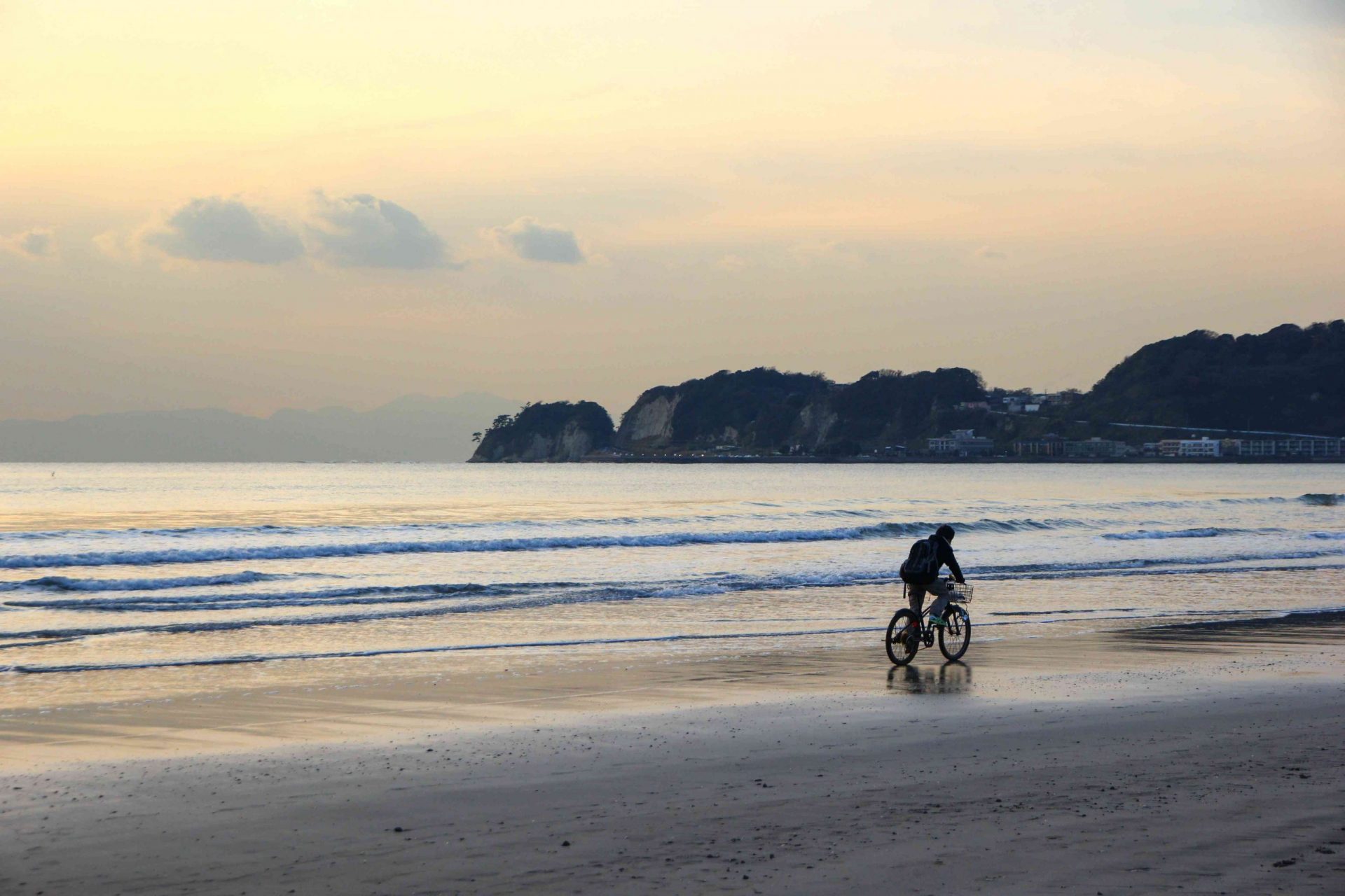 una persona monta en bicicleta a lo largo de la orilla del océano al atardecer con una formación de colinas al fondo