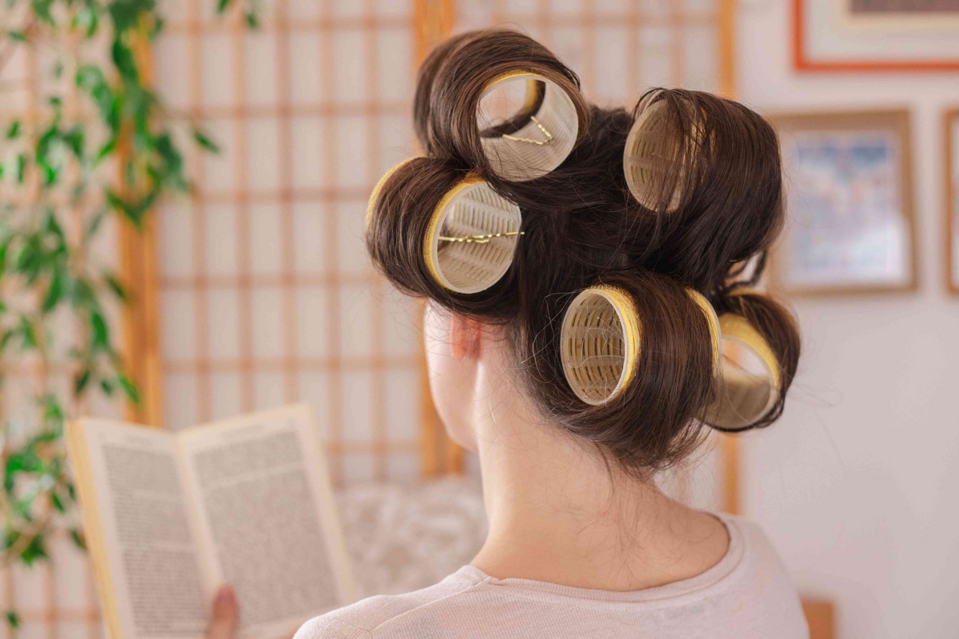 foto de espalda de una mujer leyendo un libro mientras tiene el pelo sujeto con rulos extra grandes y horquillas