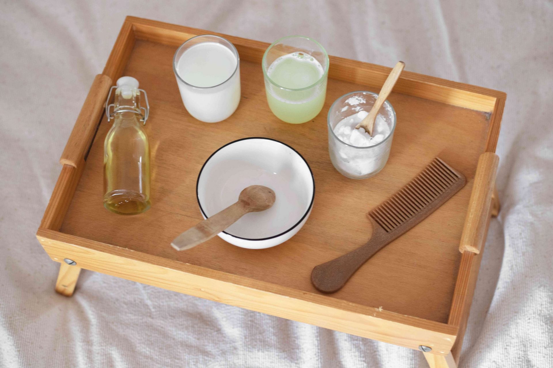 Bandeja de madera para el desayuno en cama blanca con varios ingredientes de mascarillas naturales para el pelo DIY y peine