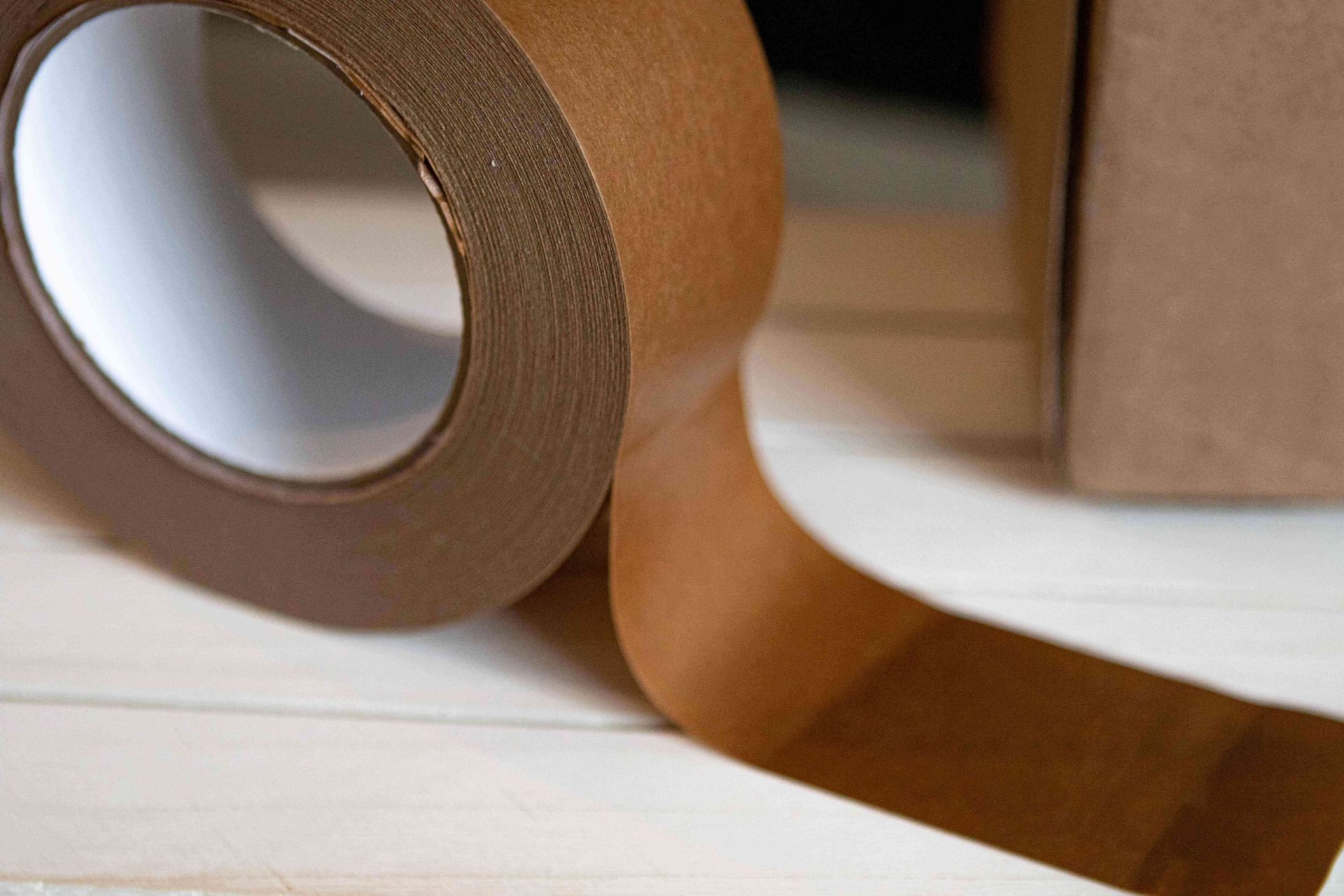 rollo de cinta adhesiva reciclable marrón con una tira pegada a la superficie blanca