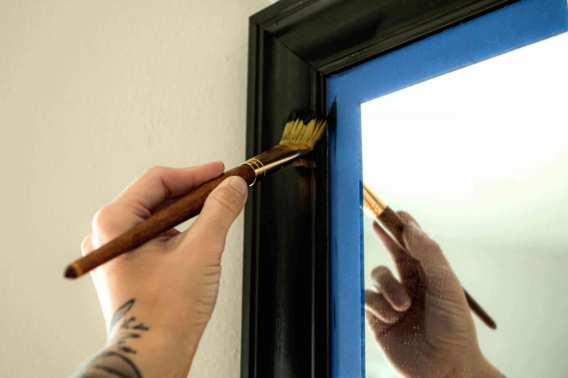 La cinta de pintor azul está pegada al espejo mientras una persona pinta el marco de negro con un pincel