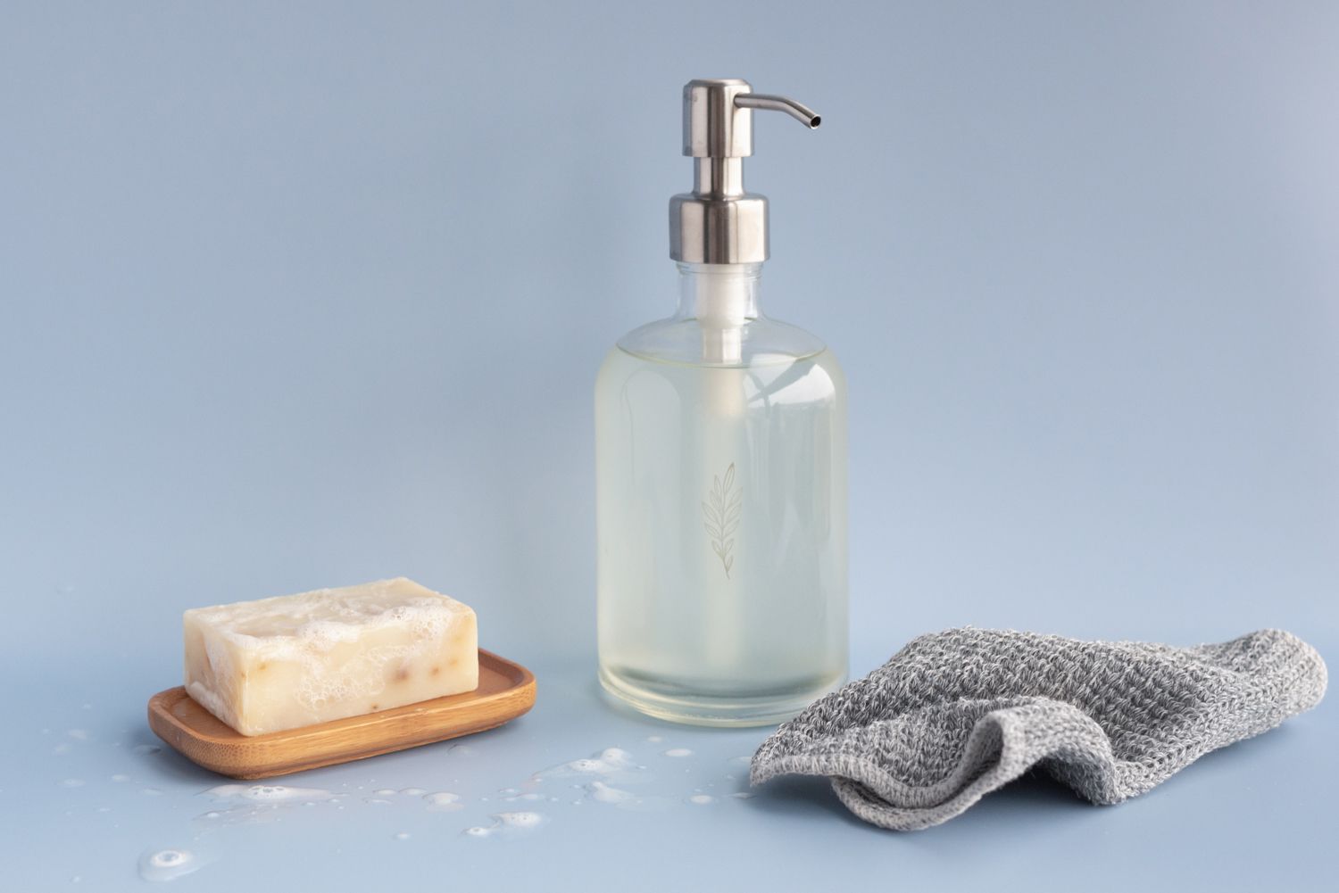 pastilla de jabón en crema en un soporte junto a un recipiente de cristal reutilizable de jabón líquido