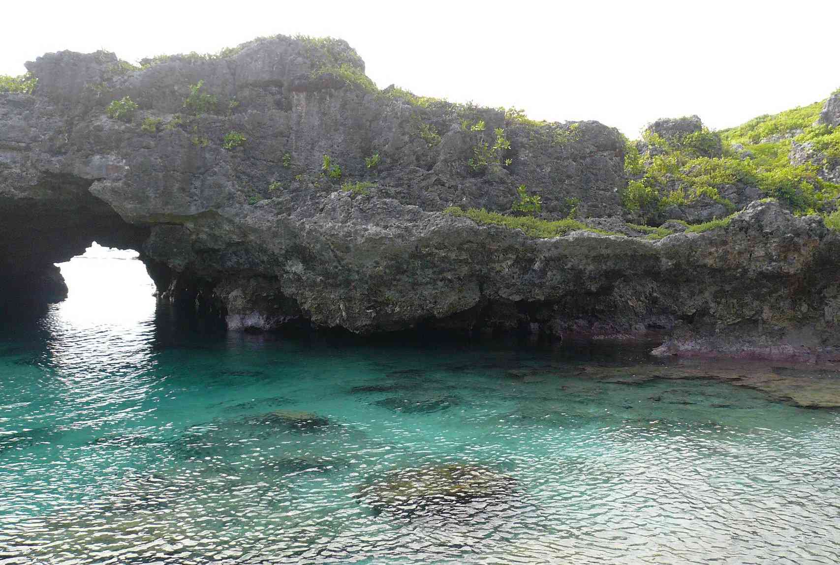Una formación rocosa arqueada se extiende sobre aguas claras y tropicales