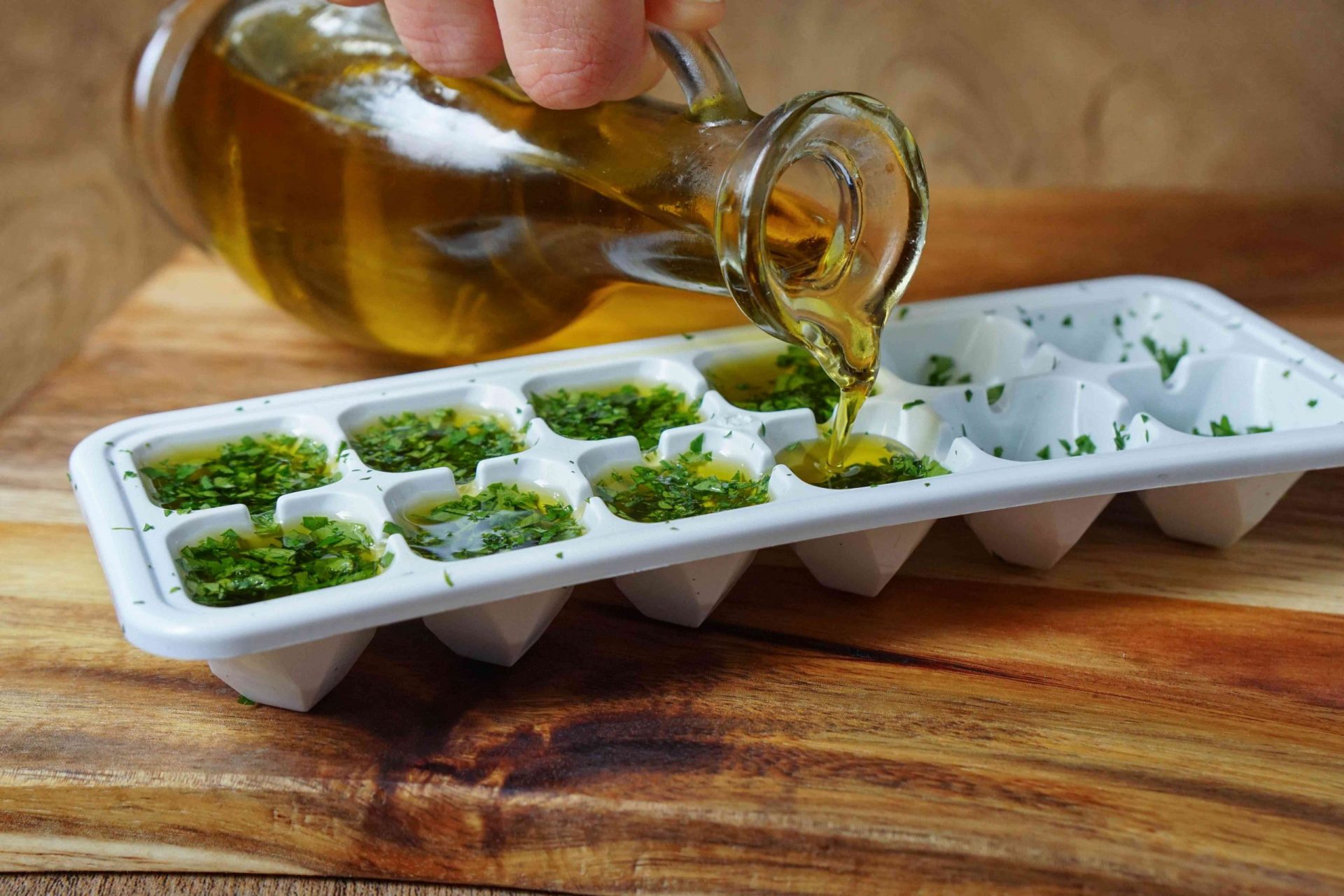 el aceite de oliva se vierte desde una jarra de cristal en una cubitera llena de perejil picado para conservarlo