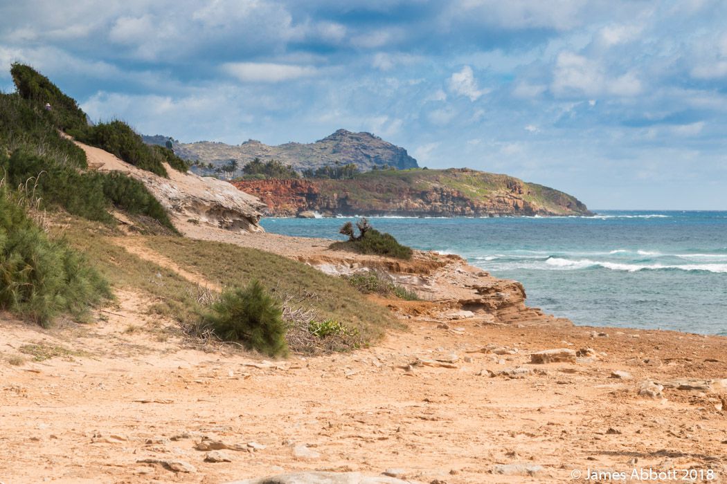 La arena rocosa y rojiza de la Playa del Naufragio se encuentra con las aguas del océano en un día parcialmente nublado