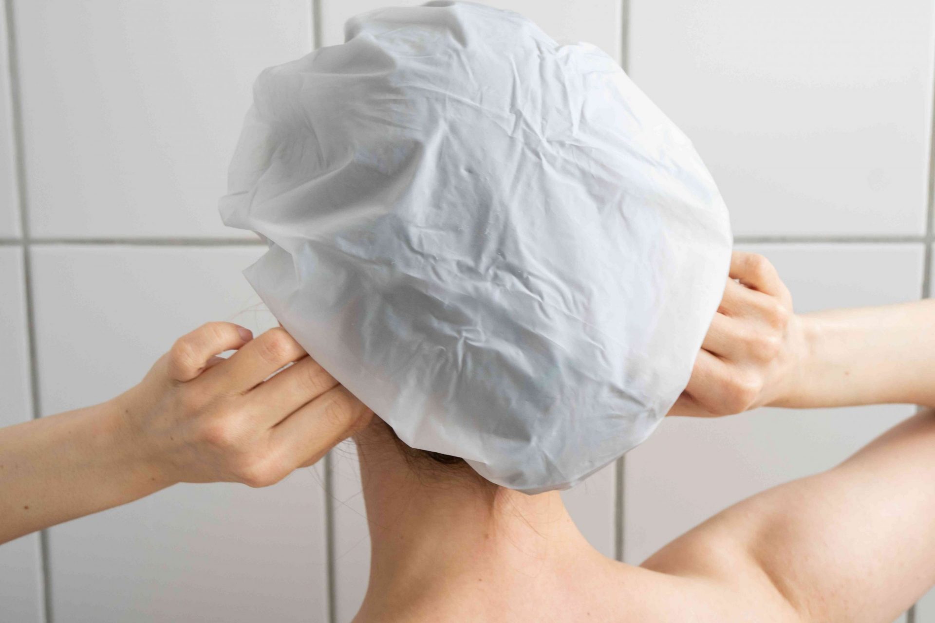 plano posterior de una persona en la ducha poniéndose el gorro de ducha blanco