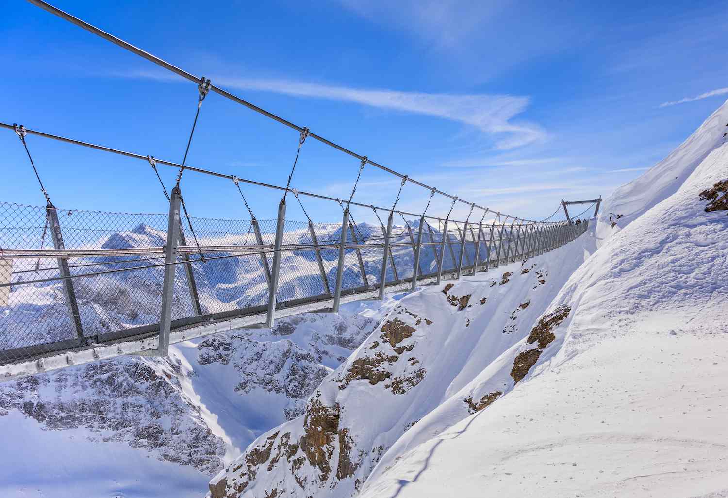 Un puente de cables de acero atraviesa un paisaje montañoso nevado