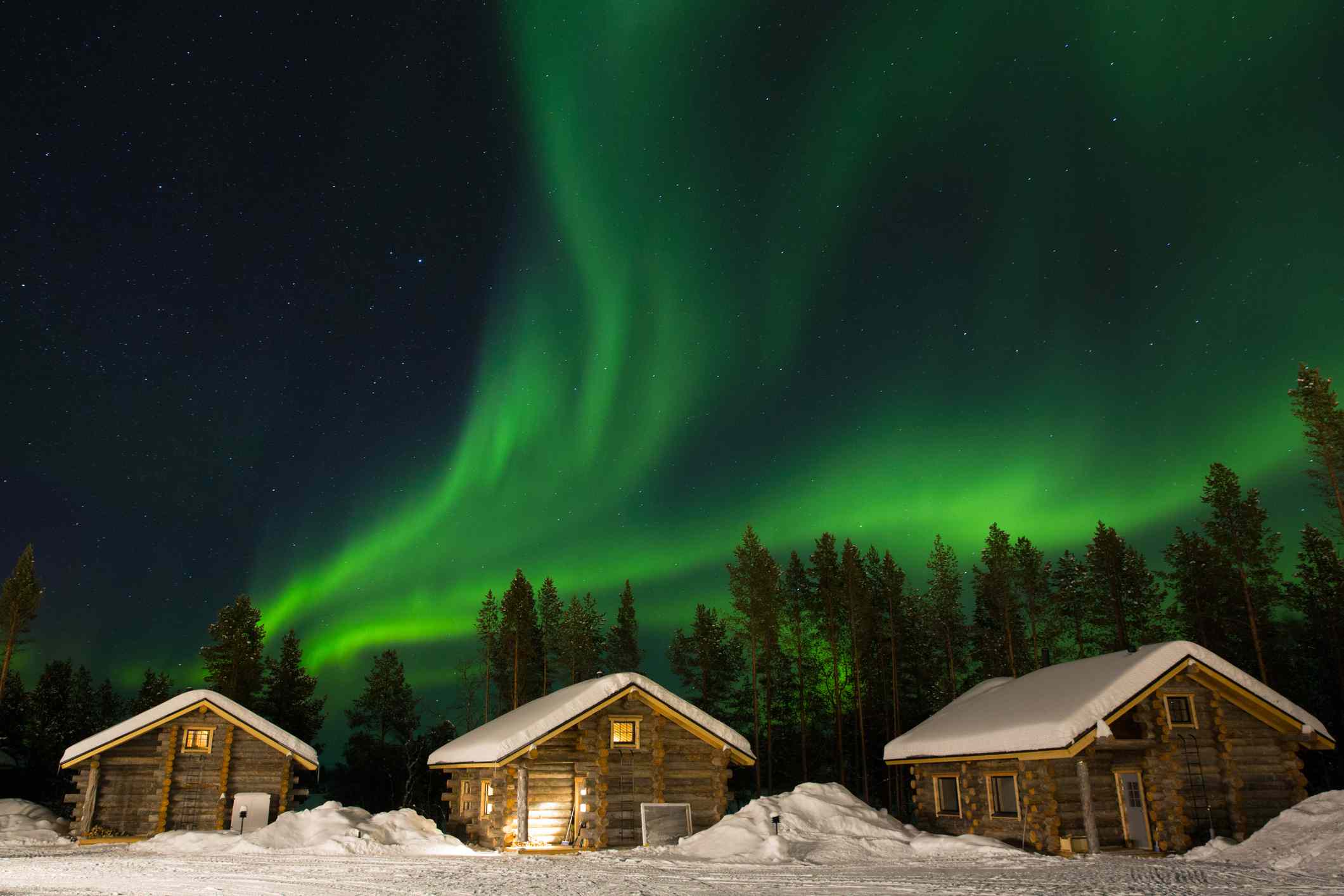 Luces verdes del norte sobre cabañas cubiertas de nieve en Laponia, Finlandia