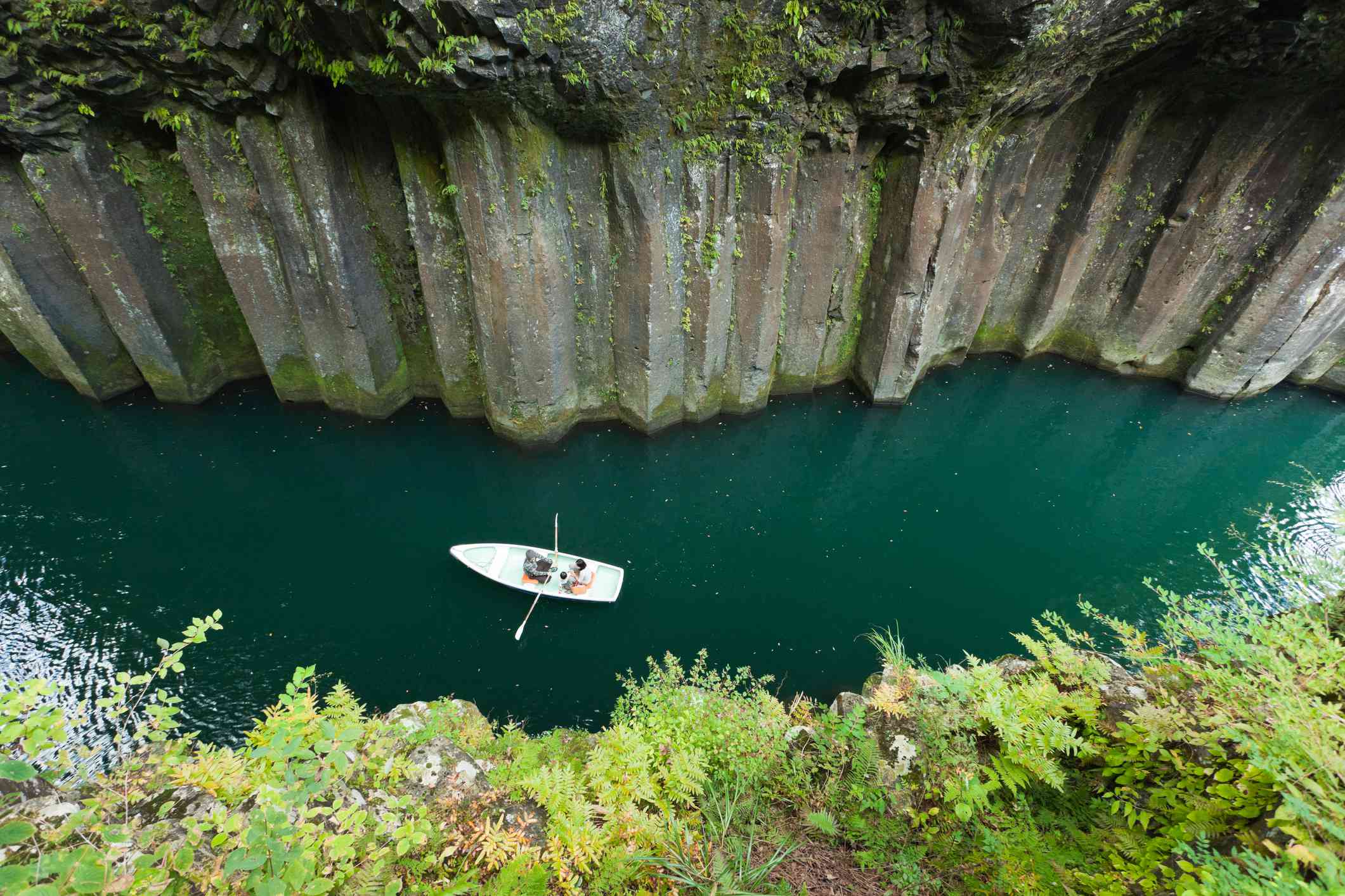 Barco remando por el río volcánico a la sombra de las columnas de basalto