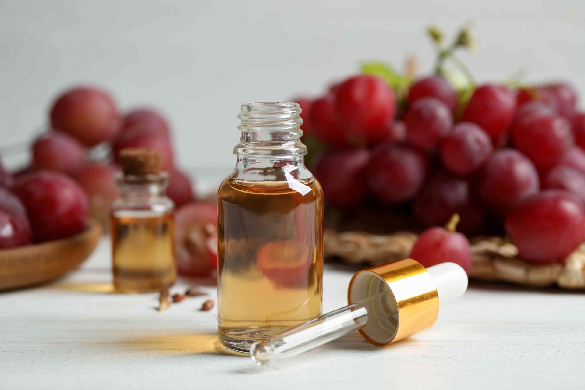 Botella de aceite natural de semillas de uva sobre mesa de madera blanca. Cosmética ecológica