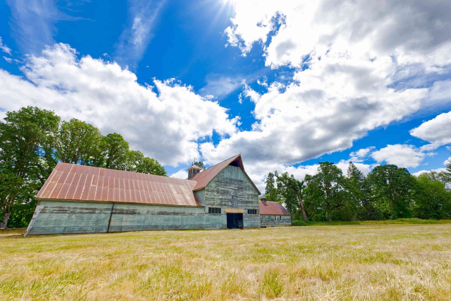 vieja granja con tejado metálico con hierba blanqueada por el sol y cielo azul soleado