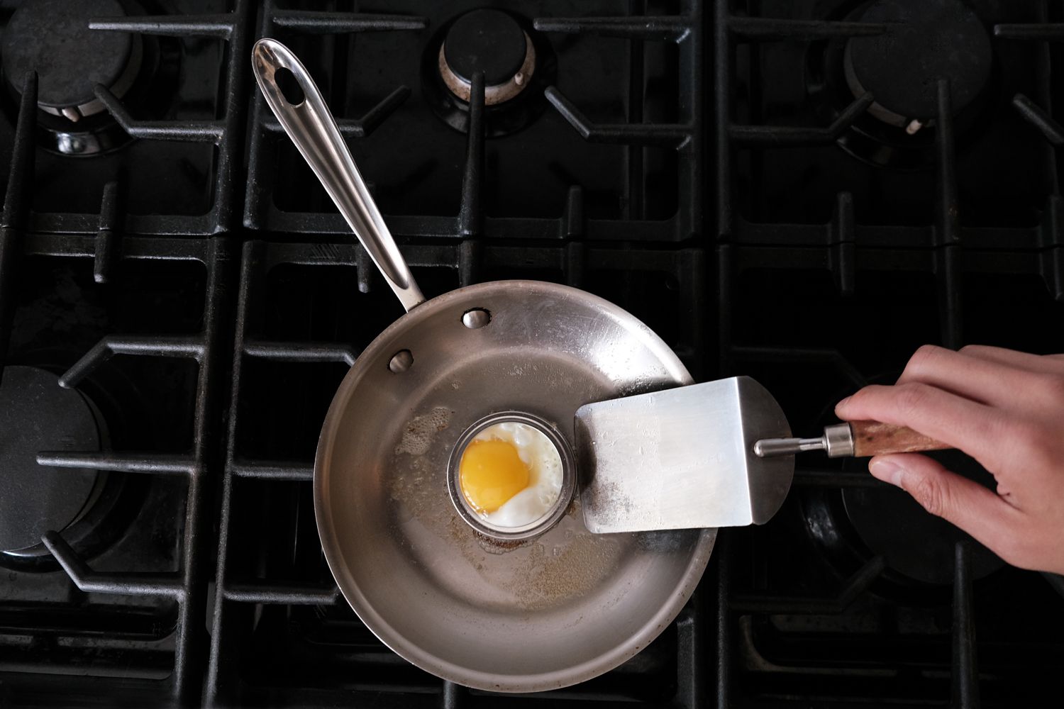 la tapa de una lata vieja se utiliza como soporte para huevos en una sartén de acero sobre la estufa