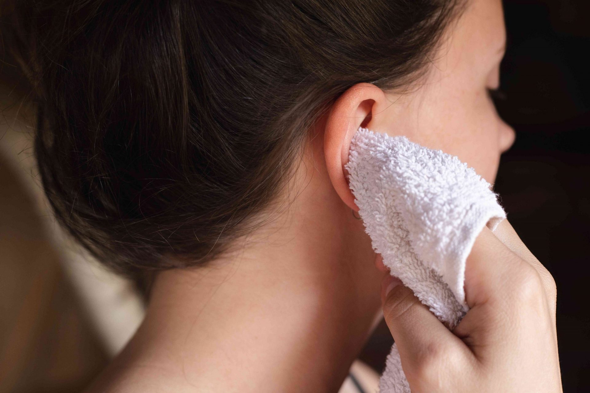 una mujer utiliza un paño blanco envuelto en un dedo para secar suavemente las orejas