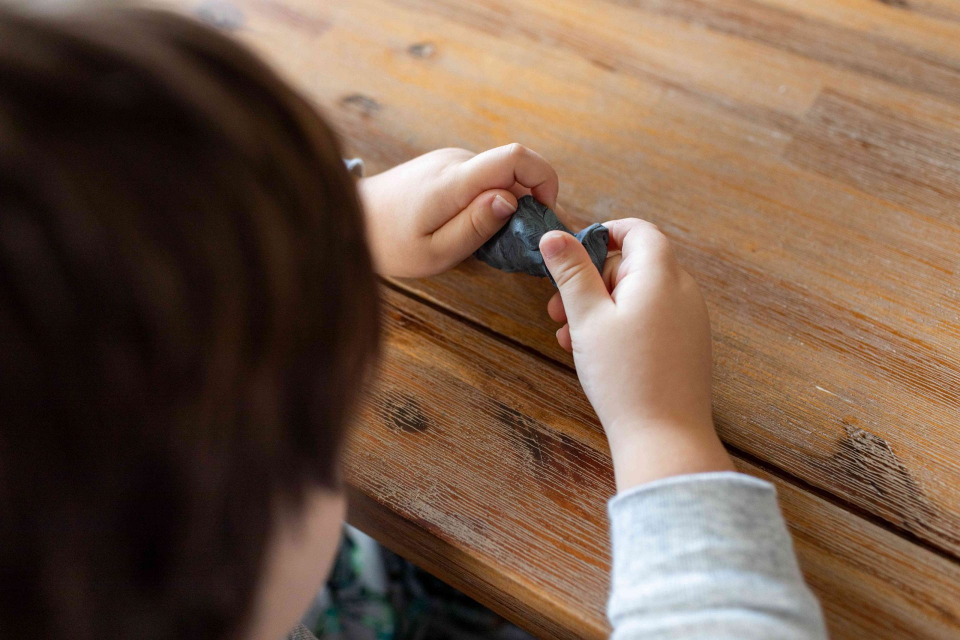 niño pequeño juega con arcilla casera de pelusa de secadora gris sobre una mesa de madera