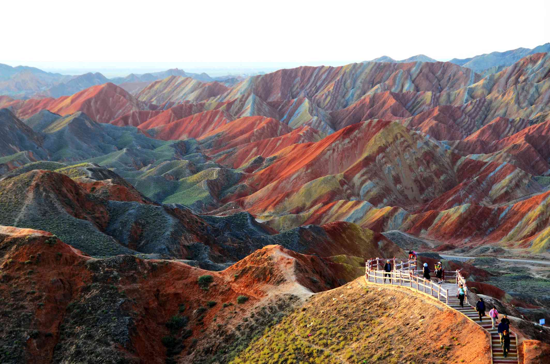 Turistas en un sendero contemplan un paisaje de montañas rayadas de rojo, azul y amarillo