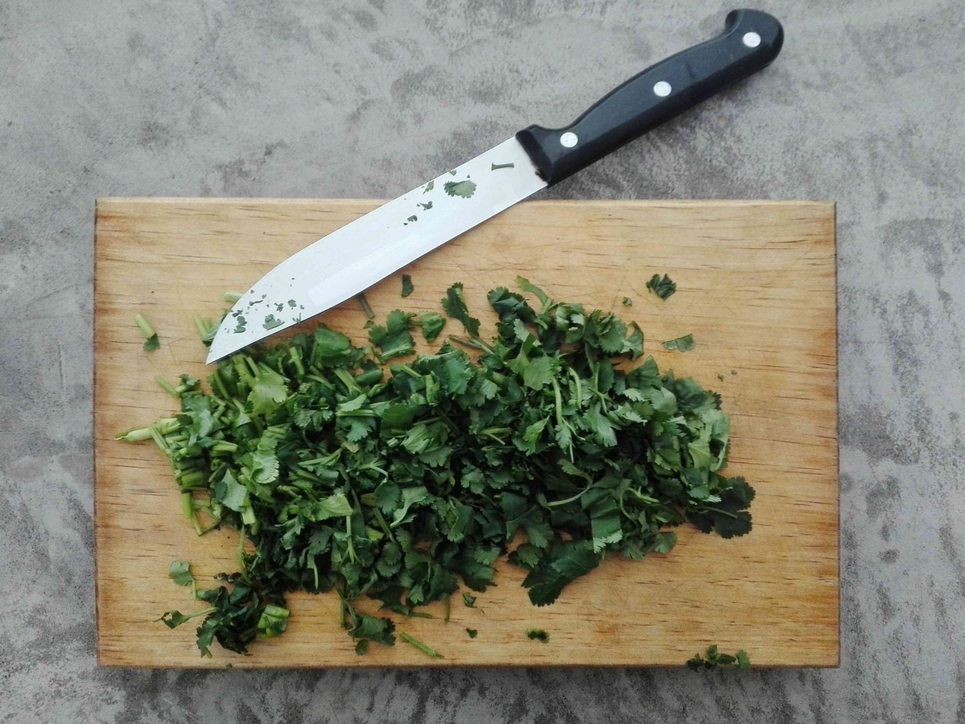 Vista directa del cilantro picado por el cuchillo en la tabla de cortar