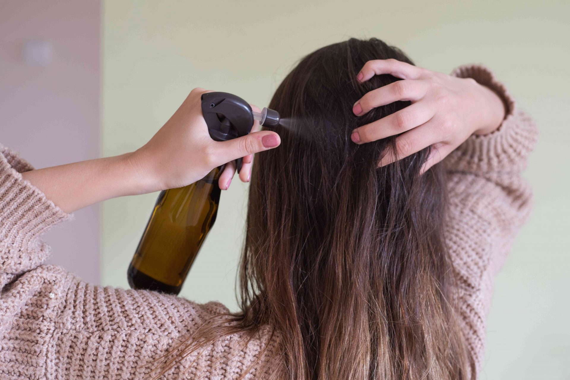 una mujer rocía la parte posterior del cuero cabelludo con vinagre de sidra de manzana en una botella de cristal para evitar la caspa