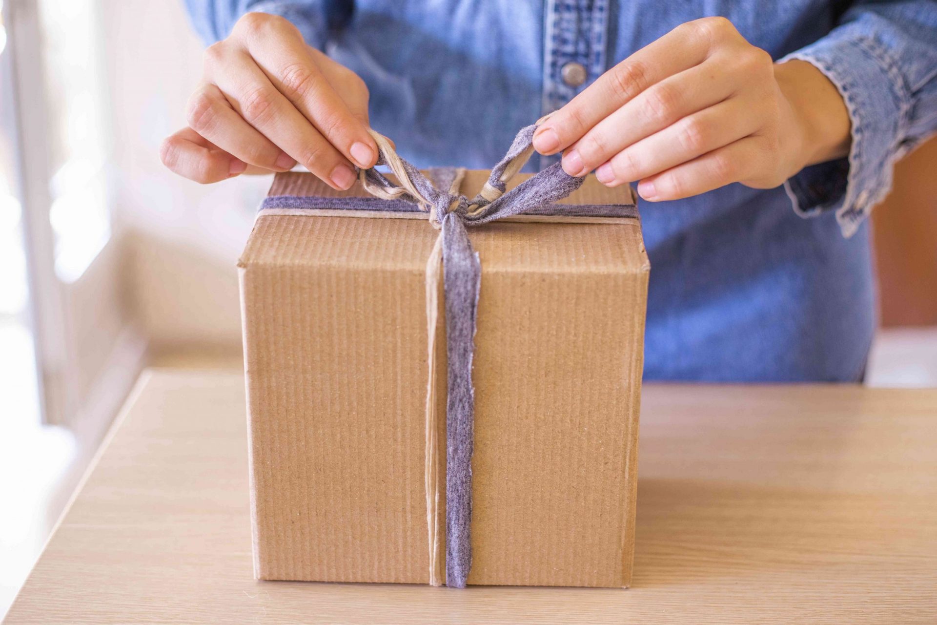 mujer con camisa vaquera ata un lazo con restos de tela en un regalo en caja