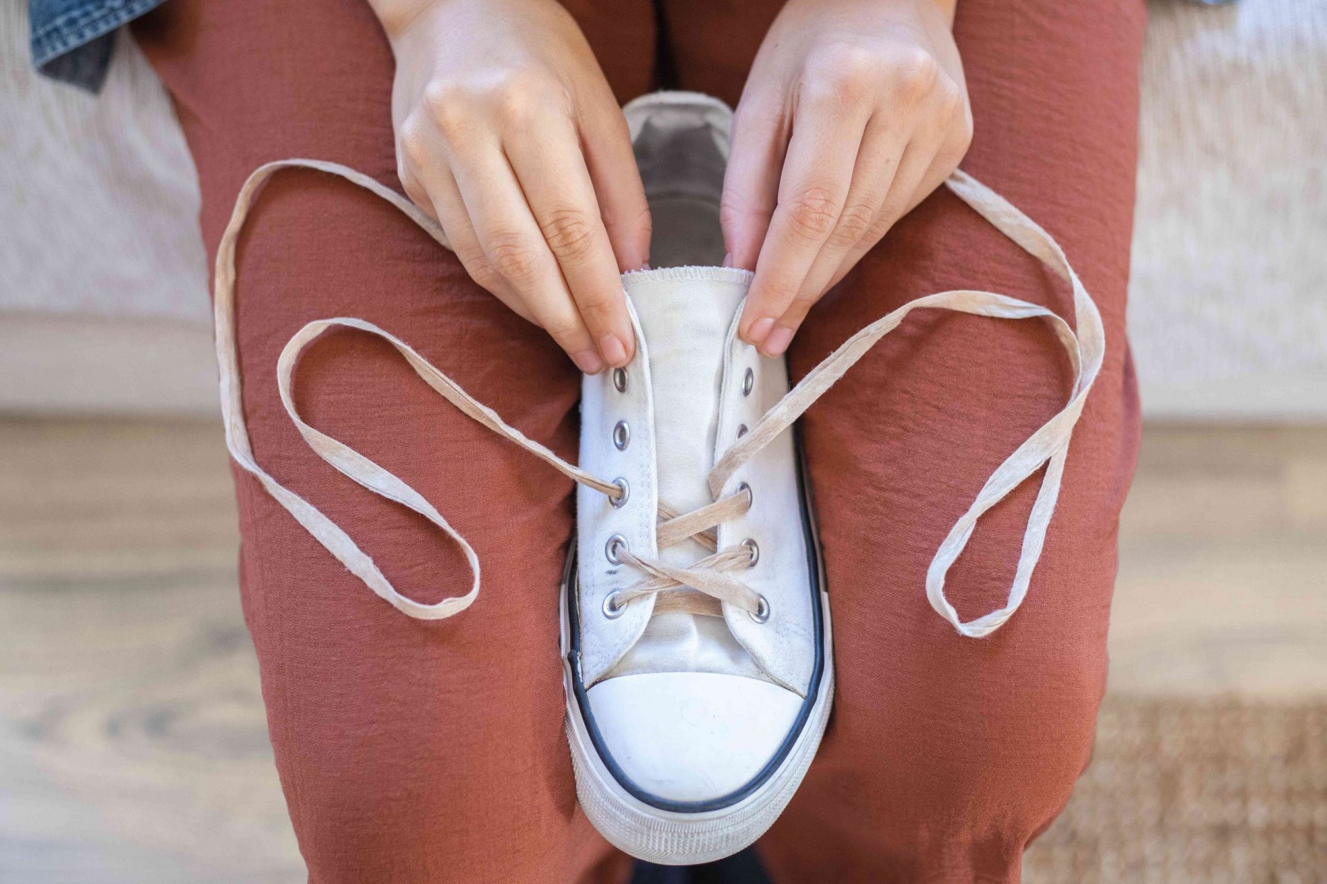 una persona ensarta restos de tela en unas zapatillas converse blancas como cordones reciclados
