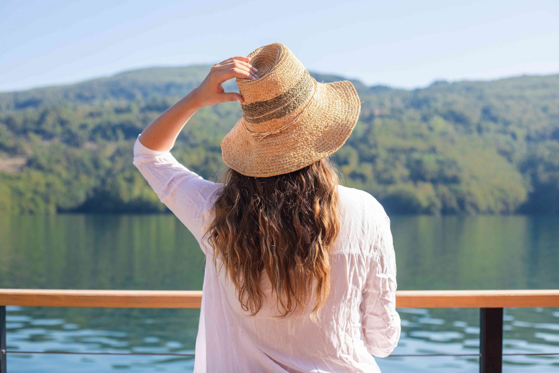 una mujer se pone un gran sombrero de paja para protegerse el pelo mientras mira el lago