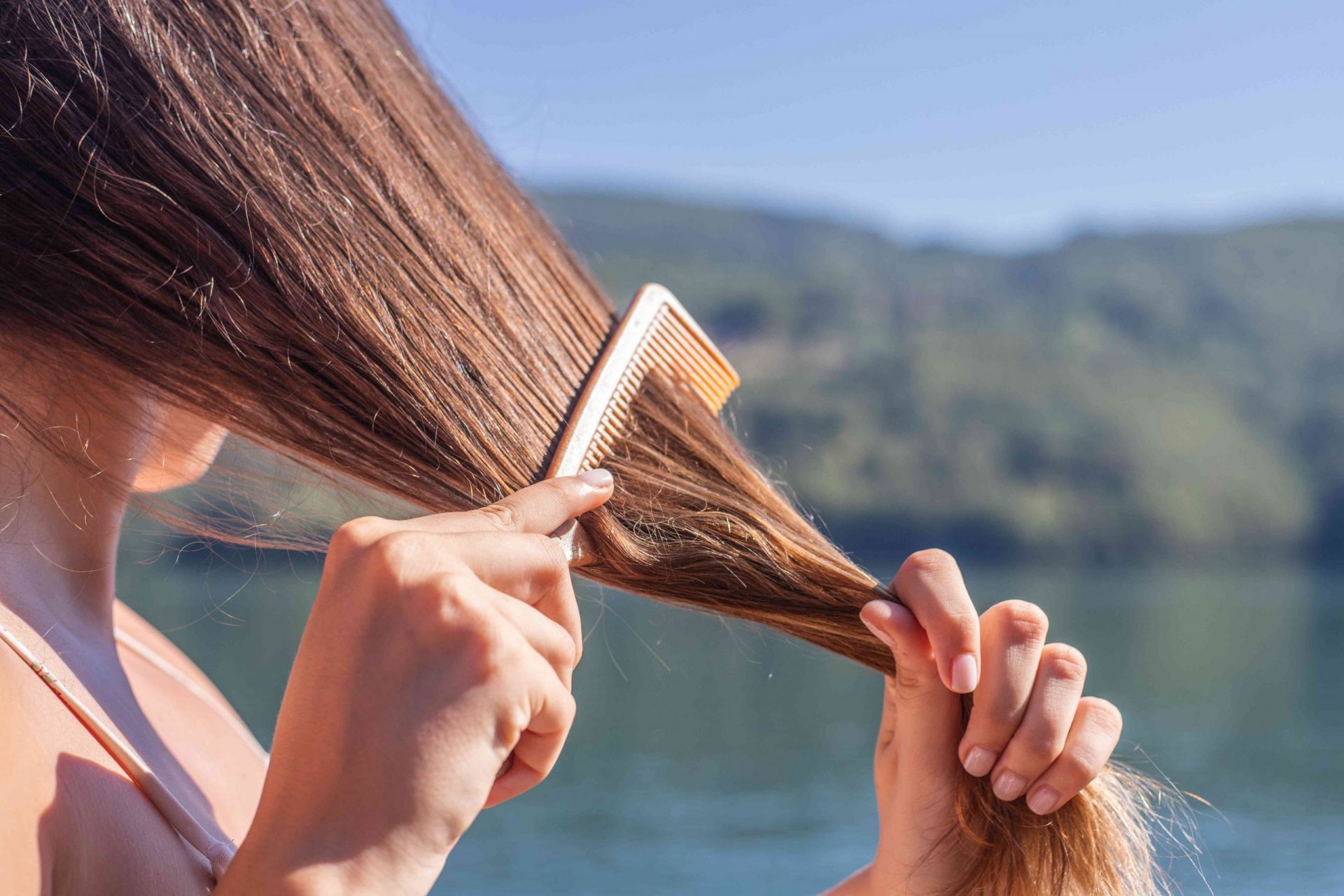 una mujer utiliza un peine de púas anchas en su pelo largo mientras está en el lago