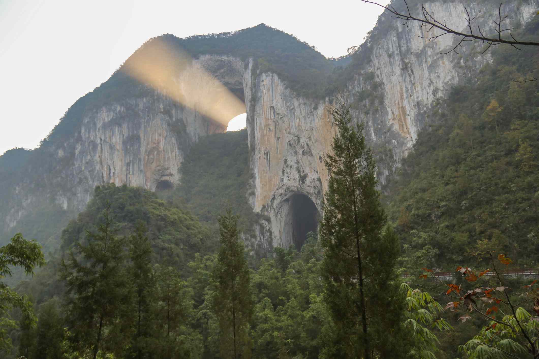 Una cresta montañosa boscosa con un arco natural y un rayo de sol que sale del arco